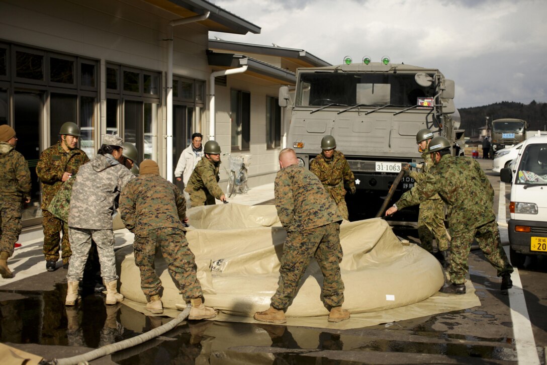 Marines from Task Force Fuji and Marine Wing Support Squadron 171, Combat Logistics Regiment 35, and members from the Japan North Eastern Army install field showers for local Japanese families at the Oshima Community Center in Oshima, Kesennuma, Miyagi, Japan on March 26 during Operation Tomodachi.