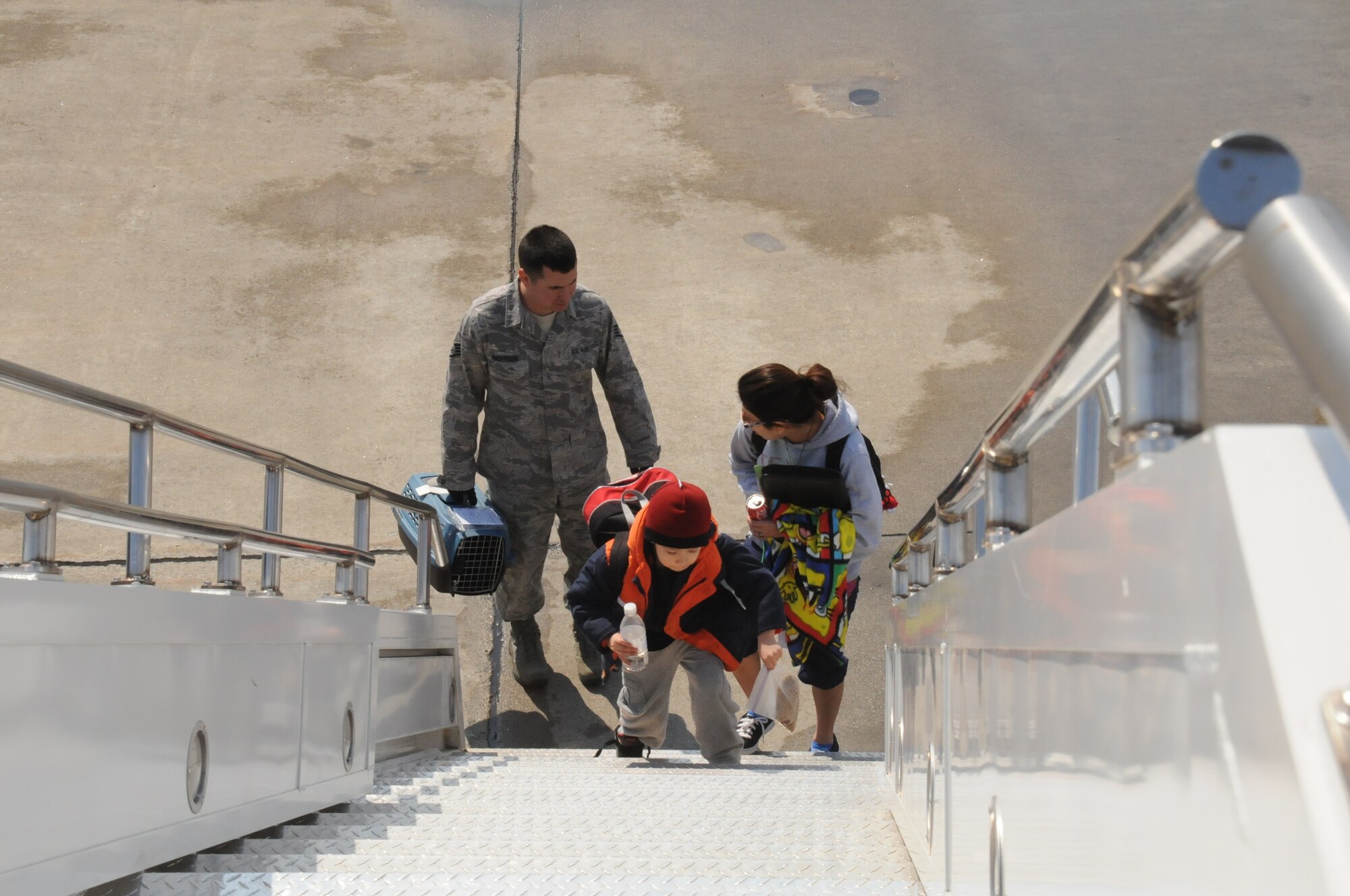 MISAWA AIR BASE, Japan -- Staff Sgt. James Anderson, 35th Logistics Readiness Squadron, carries a family pet for Belinda Sanchez and her 5-year-old son, Damian, as they board a plane headed for the U.S., March 25. Mrs. Sanchez, wife of Airman 1st Class Emanuel Sanchez, 35th Maintenance Squadron, elected to take part in the voluntary process the previous day. Mrs. Sanchez will stay with family in Texas and plans on returning to Misawa as soon as possible. (U.S. Air Force photo by Staff Sgt. Rachel Martinez/Released)