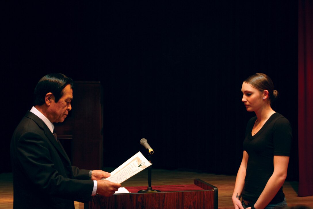 Nago City’s Superintendent of Schools, Keiichi Higa, presents a certificate of appreciation to Lance Cpl. Iris B. Brewer, an ammunition technician with Ammunition Company, 3rd Supply Battalion, Combat Logistics Regiment 35, 3rd Marine Logistics Group, III Marine Expeditionary Force, at the Nago Civic Center in Nago City, Okinawa, March 28 for volunteering to teach kindergarteners how to speak English.