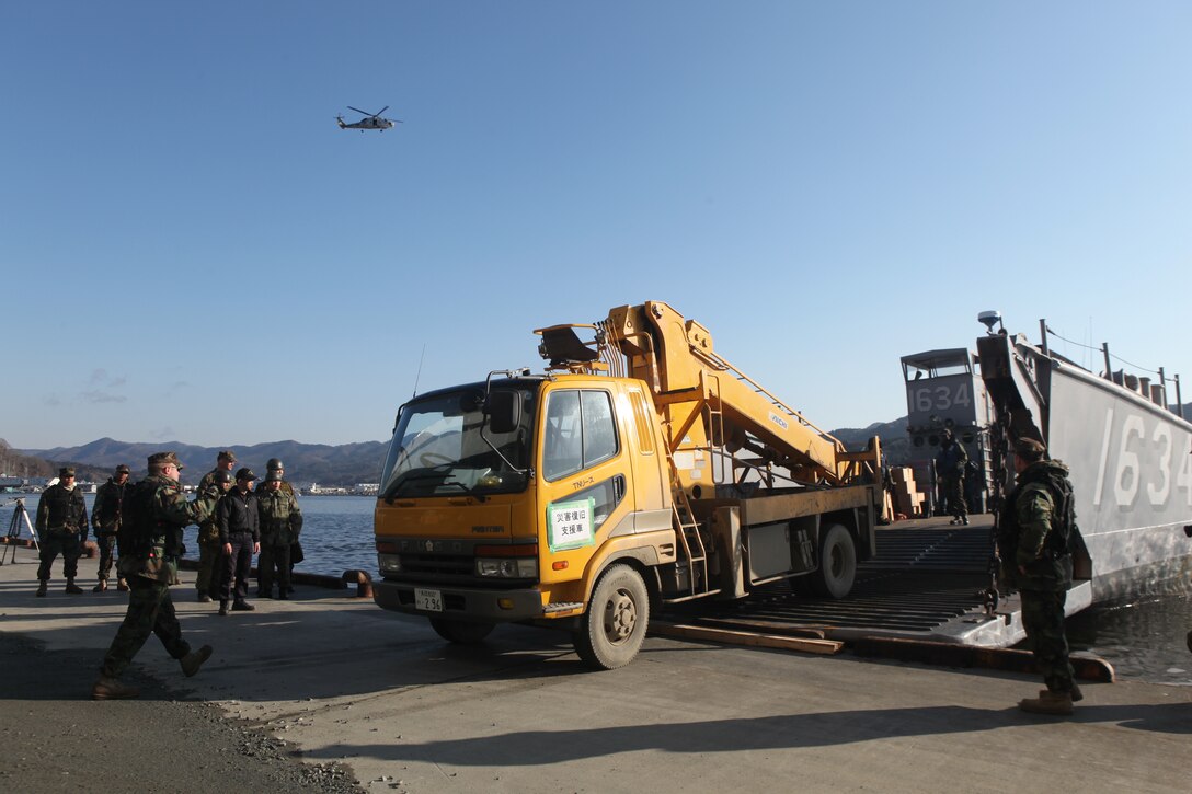 Sailors with Amphibious Squadron 11 direct Japanese utility repair vehicles into a U.S. Navy landing craft at the dock here, March 27.  The 31st Marine Expeditionary Unit and Amphibious Squadron 11 picked up the vehicles from the port here and delivered food, water, comfort items and the vehicles to residents on the isolated island of Oshima.  The island of Oshima has been cut off from the mainland since the earthquake and tsunami March 11.  U.S. Navy landing craft were used in the operation, demonstrating the MEU’s expeditionary capabilities in ship-to-shore. amphibious operations. Marines and Sailors of the 31st MEU are conducting humanitarian aid and disaster relief missions in northeast Japan assisting the Japanese Self Defense Forces in their ongoing operations.