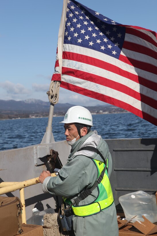 Sasaki Masaetsu, city maintenance manager, and the person in charge of restoring electrical service on the isolated island of Oshima, rides a U.S. Navy landing craft carrying Japanese utility repair vehicles.  The 31st Marine Expeditionary Unit and Amphibious Squadron 11 picked up the vehicles from the Kessenuma port and delivered food, water, comfort items and the vehicles to assist in restoring power.  The island of Oshima has been cut off from the mainland since the earthquake and tsunami March 11.  The operation demonstrated the MEU’s expeditionary capabilities in ship-to-shore amphibious operations. Marines and Sailors of the 31st MEU are conducting humanitarian aid and disaster relief missions in northeast Japan assisting the Japanese Self Defense Forces in their ongoing operations.