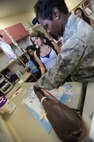 Tech. Sgt. Shanandoah Derrico, NCO-in-charge  of Family Health, demonstrates how to place an IV on a test arm for Radford High School students Mar. 24 at the 15th Medical Group during a tour of various facilities at Joint Base Pearl Harbor-Hickam, Hawaii. During the visit, the RHS students visited various locations on base including the C-17 Operations building, C-17 simulator, fitness center, and the child development center. (U.S. Air Force photo by Airman 1st Class Lauren Main)