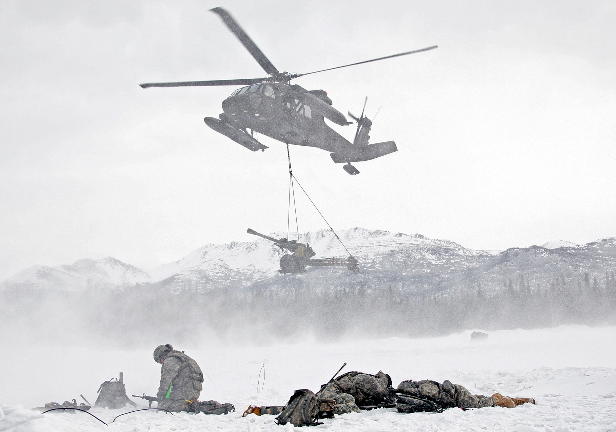 Soldiers from Alpha Battery 2-377 PFAR hunker down as  an Alaska Army National Guard UH-60 Blackhawk prepares to lower a M119A2 Howitzer during an air assault raid at LZ Ranger.