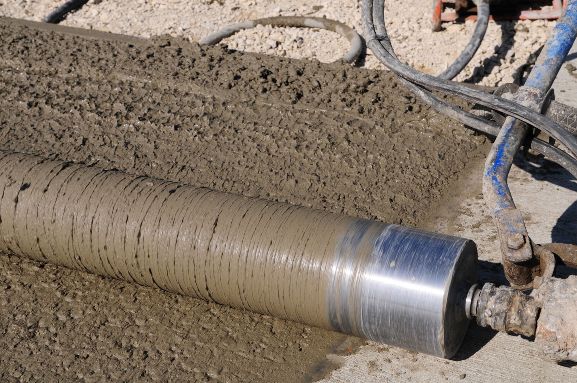 RAF MILDENHALL, England -- A razorback screed roller spins round as it gets pulled along wet concrete here to smooth it out March 24, 2011. The area is being transformed into a batching plant to mix concrete on base, rather than at an off site location. A storage area, mixing plant and silos were also added on site. About 2.4 British tons (2240 pounds) of concrete can be mixed in about 30 seconds, and having the plant on base will help speed up projects including the hardstands, which will be resurfaced later this year. (U.S. Air Force photo/Karen Abeyasekere)