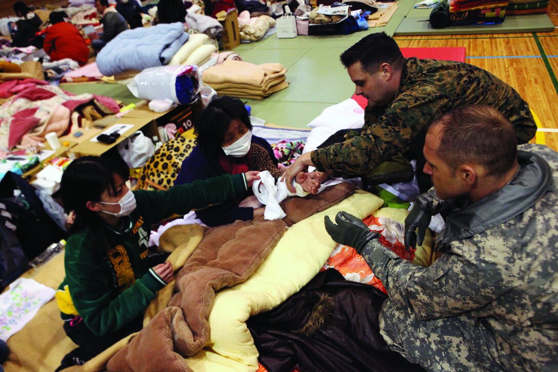 U.S. Navy Lt. Cmdr. Ewell Hollis, physician with 3rd Marine Expeditionary Brigade (Forward), examines a Japanese woman here March 21 who broke her arm during the tsunami. Service members with United States Forces Japan (Forward) and Japanese East Army surveyed the Shiogama City Gymnasium to establish shower, power, food, and water supply needs. The gymnasium is being utilized as an internally displacement person camp for residents affected by the earthquake and tsunami March 11.
