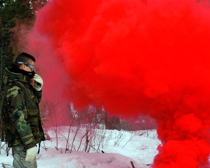 A survival, evasion, resistance and escape student from Fairchild Air Force Base, Wash., pops red smoke March 13, 2011, in anticipation of a rescue helicopter during vector training in Colville National Forest, Wash. The vector training gets students familiar with proper protocol to correctly guide a helicopter into position to safely rescue them if needed. This entails everything from authentication, to using a compass to pinpoint their heading for the pilot to be able to locate them. (U.S. Air Force photo/Tech. Sgt. J.T. May III)