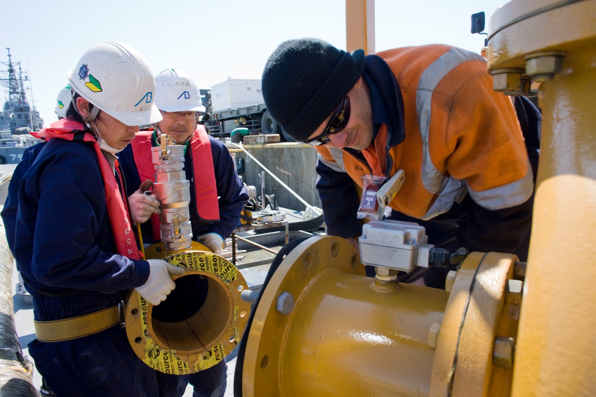ONAHAMA, Japan -- Contractors from theTokyo Electric Power Company and Blair Smith, from the REL Group in Australia, piece together a water pump system to transport fresh water into the Fukushima nuclear power plant March 28, 2011. The system of high pressure pumps and hoses will be used to spray freshwater from barges onto the plant. Japan Maritime Self-Defense Force vessels towed the barges full of freshwater from Yokosuka to the site.  Eight Yokota Airmen designed and created necessary adapters, pressure valves and other pieces of equipment to modify the pumps for the mission. (U.S. Air Force photo/Osakabe Yasuo)