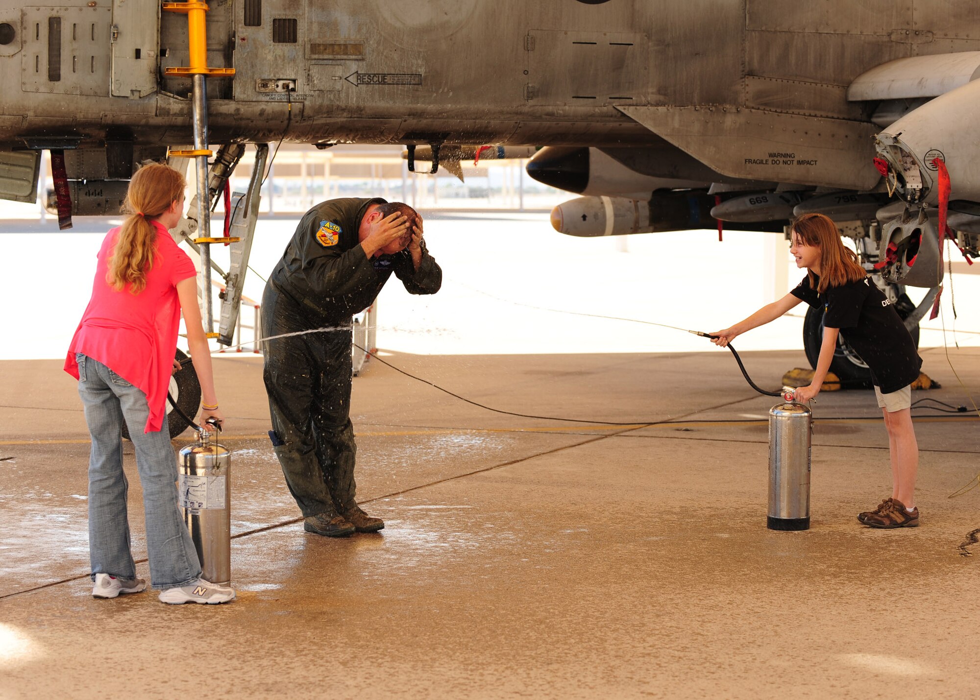 DAVIS-MONTHAN AIR FORCE BASE, Ariz. – Charlotte (left) and Emily Kapuscak, daughters of Lt. Col. Andrew Kapuscak, spray their dad with water in celebration of his 3,000th flying hour, on the flight line here April 27. (U.S. Air Force photo/Airman 1st Class Jerilyn Quintanilla)