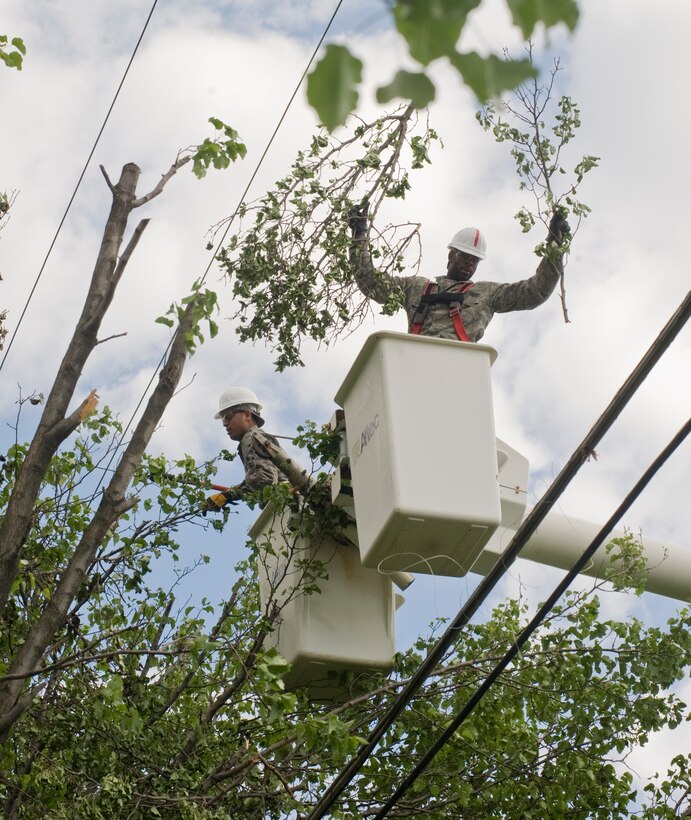 Airman 1st Class Christopher Keller, 11th Civil Engineer electrical systems apprentice, left, trims tree tops down below power lines with a hydraulic saw, as A1C Igbaji Odey, 11 CES electrical systems apprentice, tosses tree branches into a pile below for collection on West Perimeter Road April 29. The 11 CES deployed Airmen and civilian personnel to various areas around Joint Base Andrews to clean up downed trees and reenergize power lines left by recent tornado winds that briefly touched down here April 27. (Photo by Bobby Jones) 
