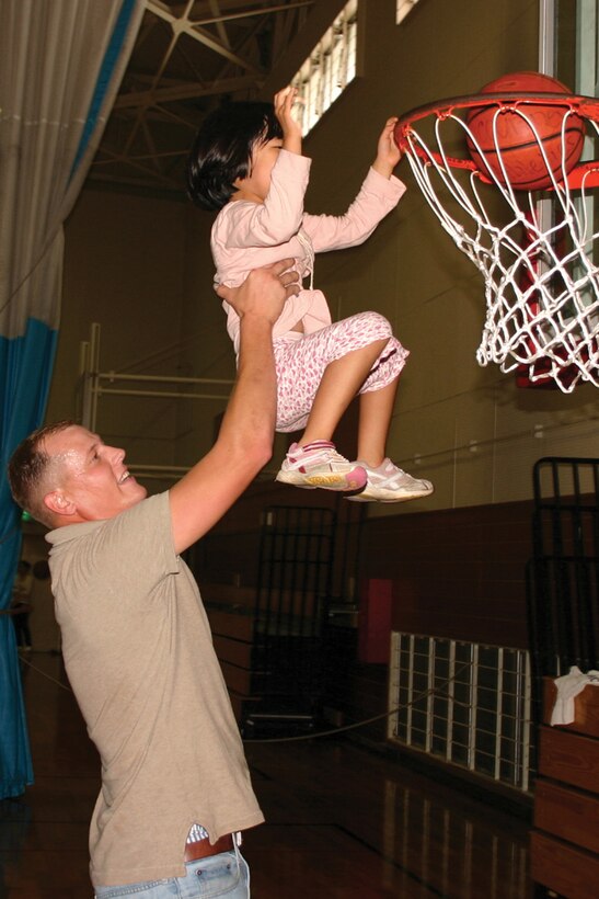 Cpl. Charles Prickett, with III Marine Expeditionary Force Civil Affairs, lifts a child, from the Wai Mentally Challenged Home, to make a basket at the Camp Courtney Ironworks Gym May 4.