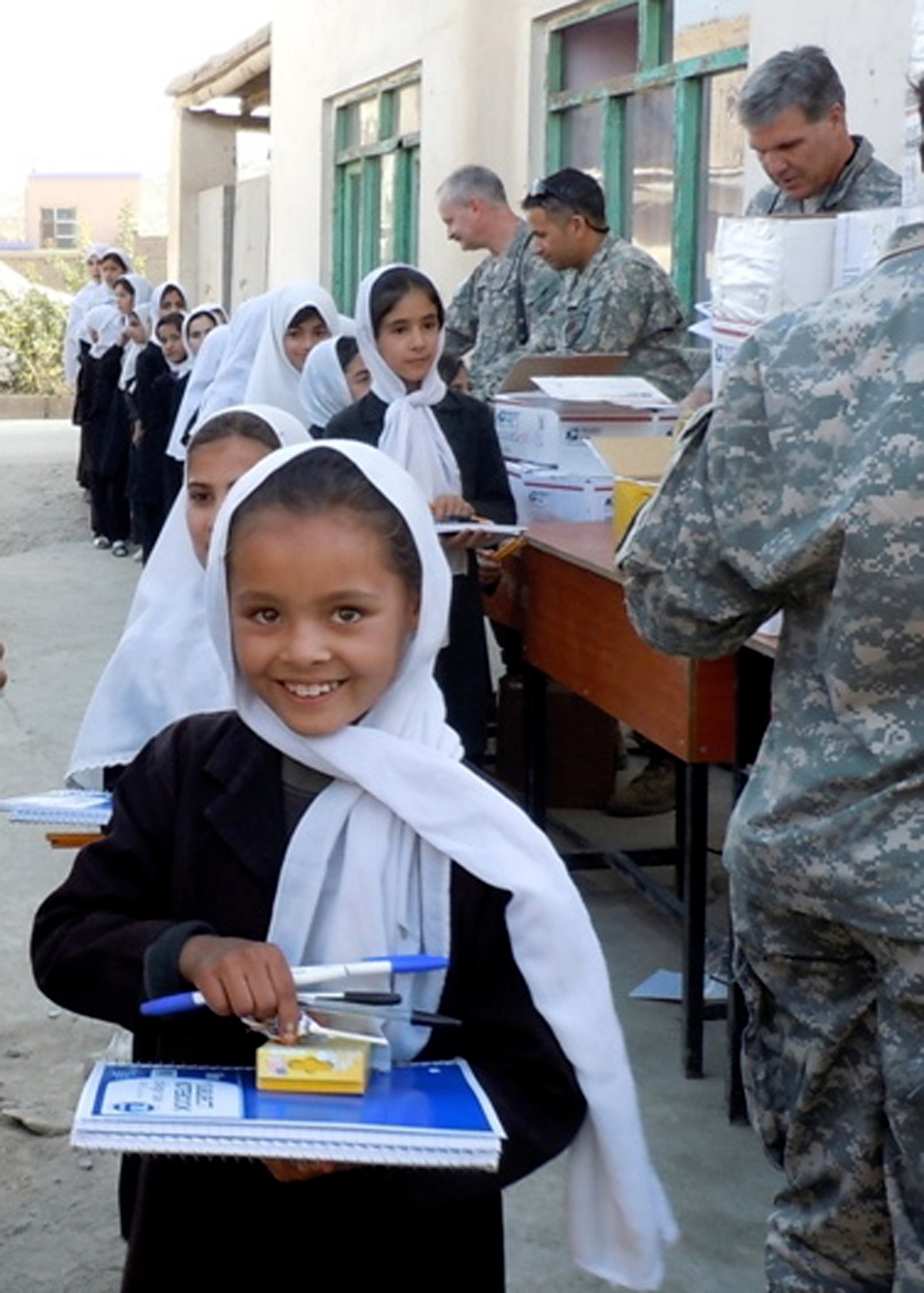 Col. Bob Wicks (top right) and other members of Regional Support Command-Capital hand out supplies to young girls at a school in Kabul, Afghanistan. Colonel Wicks and the other RSC-Capital military service members adopted a girls' school and donated tents and supplies from care packages sent by family and friends. Colonel Wicks is the Regional Support Command-Capital commander.  (Courtesy photo)