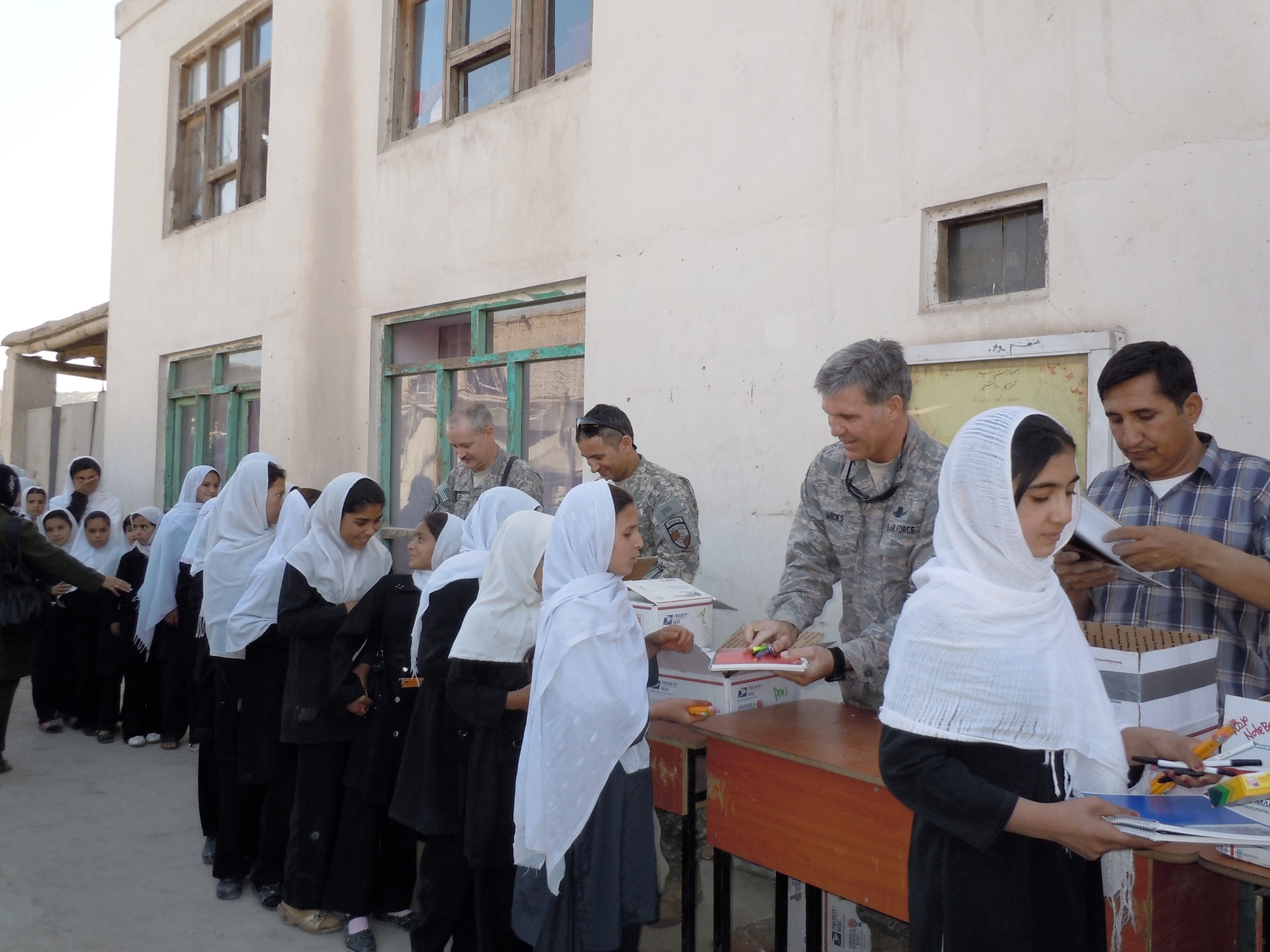 Col. Bob Wicks (top right) and other members of Regional Support Command-Capital hand out supplies to young girls at a school in Kabul, Afghanistan. Colonel Wicks and the other RSC-Capital military service members adopted a girls' school and donated tents and supplies from care packages sent by family and friends. Colonel Wicks is the Regional Support Command-Capital commander.  (Courtesy photo) 
