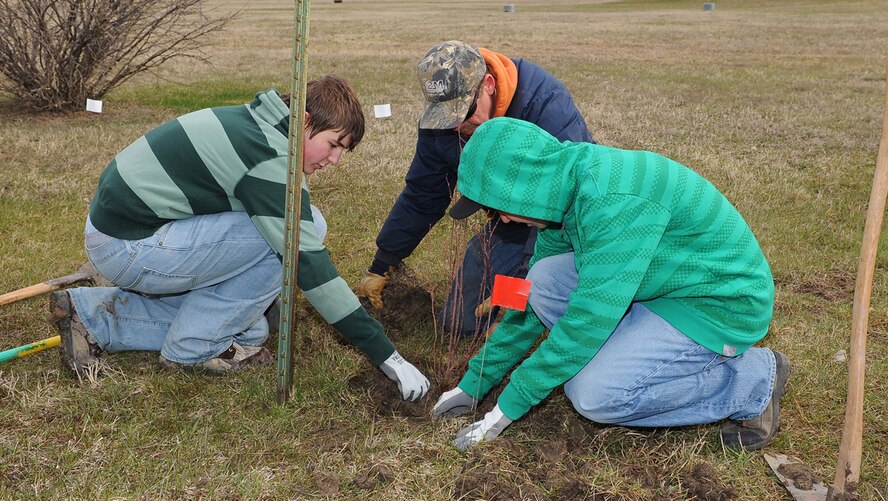 Great Falls High freshmen Gage Kuykendall (left) and Micah Forsyth (right) work with Lonnie Dalke, City of Great Falls Forester, to plant a woods rose tree at Pow Wow Park Pond on Malmstrom Air Force Base April 29. About 30 student volunteers helped plant more than 500 trees and shrubs at the park to celebrate Arbor Day. (U.S. Air Force photo/Beau Wade)