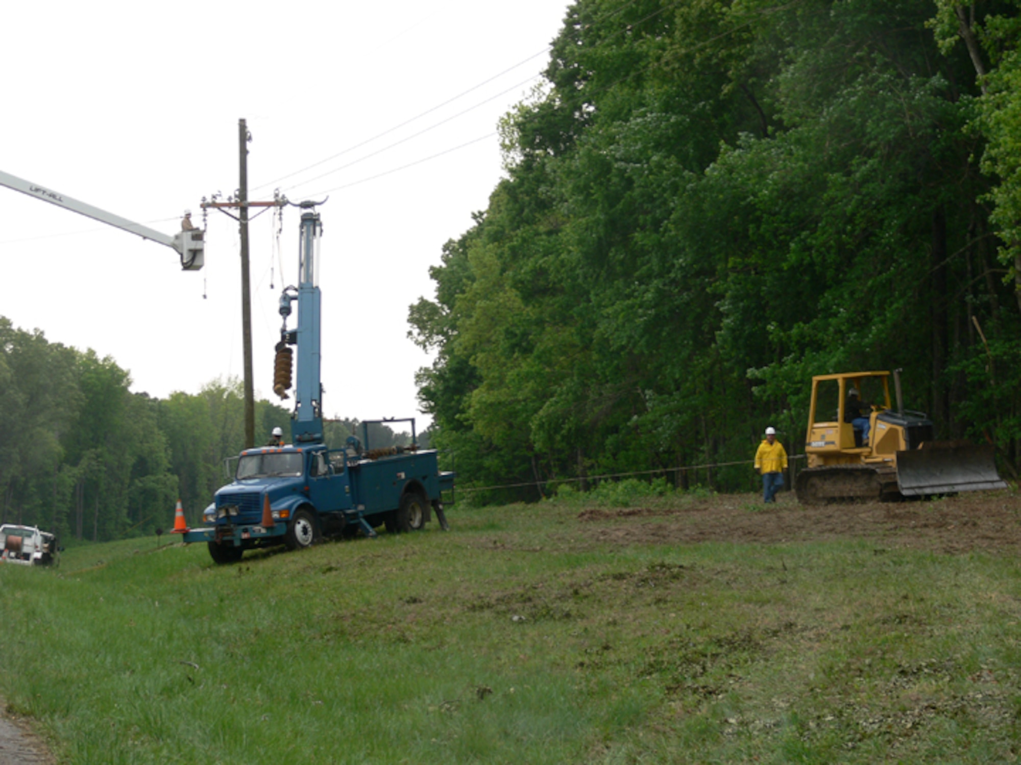 Tom Payne (in bucket), John Williams (operating the line truck) and James Melton (on the ground), all from Power Control, and James Mears (operating the bull dozer) from Roads and Grounds work on restoring electricity to the base following the April 27 storm. (Photo provided)