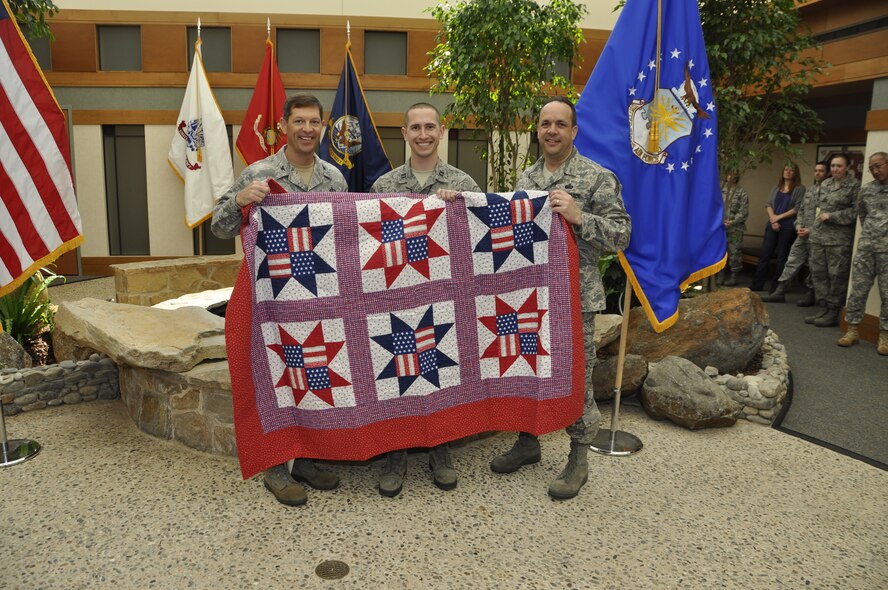 Col. Thomas C. Joyce, (left) Air Force Mortuary Affairs Operations commander and Chief Master Sgt. David Fish, (right) AFMAO enlisted manager, present Capt. Joshua Daniels a Quilt of Valor for his work at the mortuary on behalf of a grateful American. Quilters from all over the nation make quilts for individuals affected by war. (U.S. Air Force photo/Tech. Sgt. Michael Stewart)