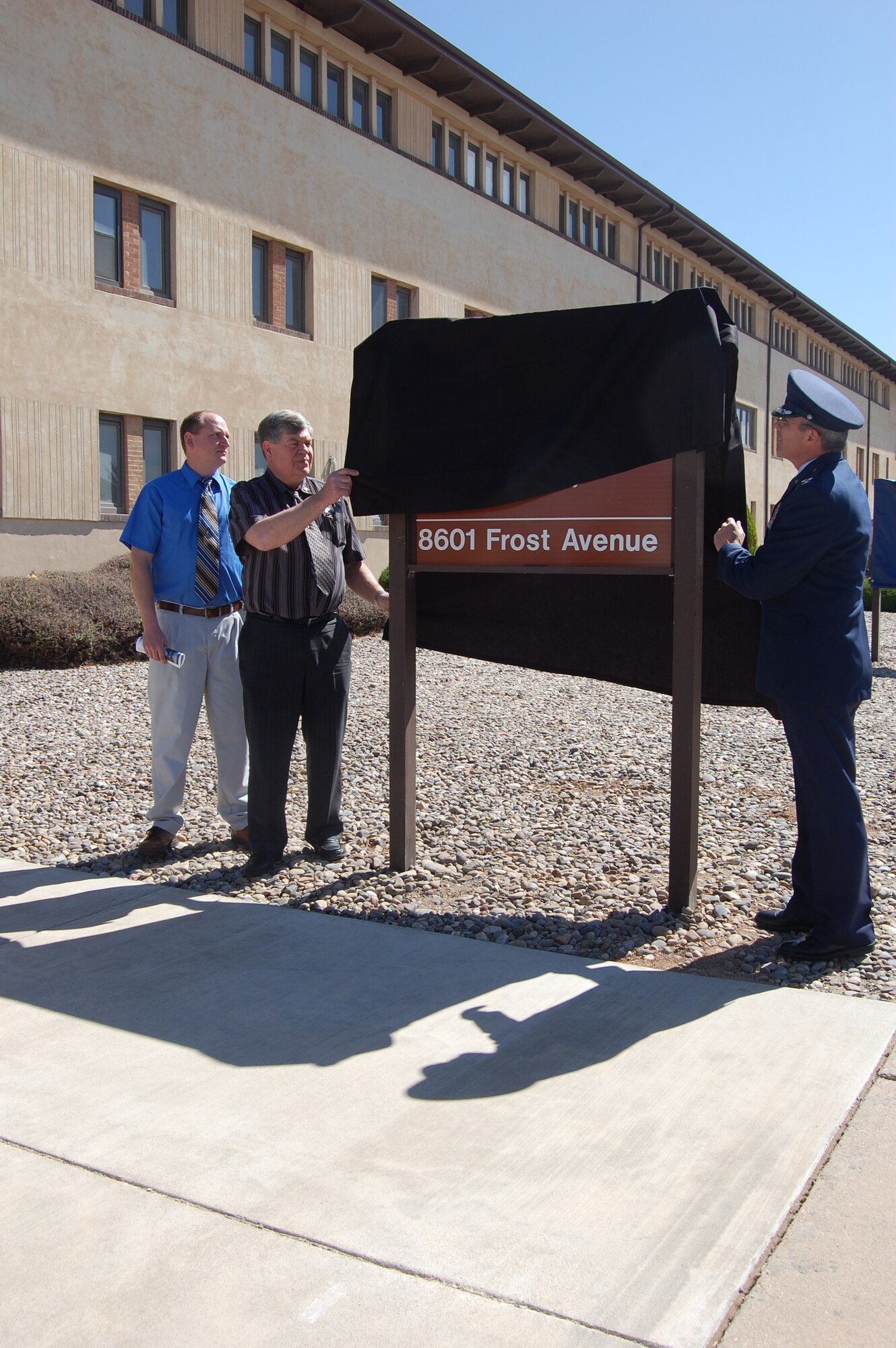 In honor of Staff Sgt. Christopher Frost, his brother and father, John and Garry Frost, left, and Col. Robert L. Maness, 377th Air Base Wing commander, unveil the sign in front of the Airman Leadership School, where Staff Sgt. Frost graduated in 2006.
