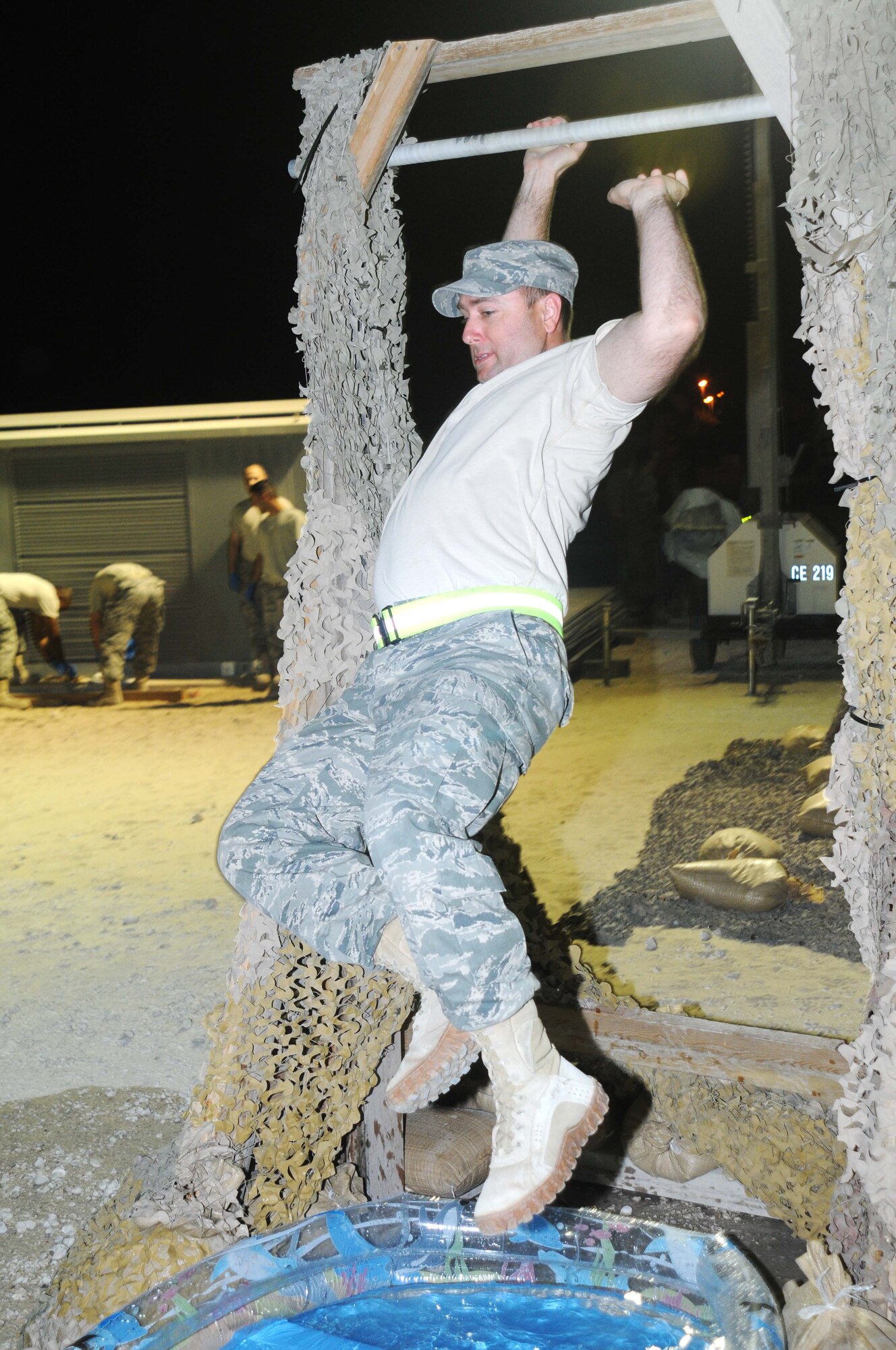 Master Sgt. Steven Erb from the 379 Expeditionary Civil Engineer Squadron swings from a bar over a pool of water May 4 in Southwest Asia. The Airmen had to go through an obstacle course beofre entering the combat dining in event. (U.S. Air Force photo/ Staff Sgt. Anthony Graham)