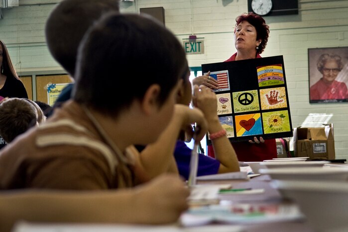 NELLIS AIR FORCE BASE, Nev. -- Mrs. Gail Schomisch, "All Fired Up" ceramics studio owner, shows Lomie Heard Elementary School students an example of a tile display on May 5. Mrs. Schomisch came to the school to help create a mural for display in the USO common room, at McCarran International Airport, Las Vegas. More than 125 students were chosen to paint pictures on the tiles for a mural that will be displayed in the USO common room at the McCarran International Airport, Las Vegas. (U.S. Air Force photo by Airman 1st Class George Goslin) 