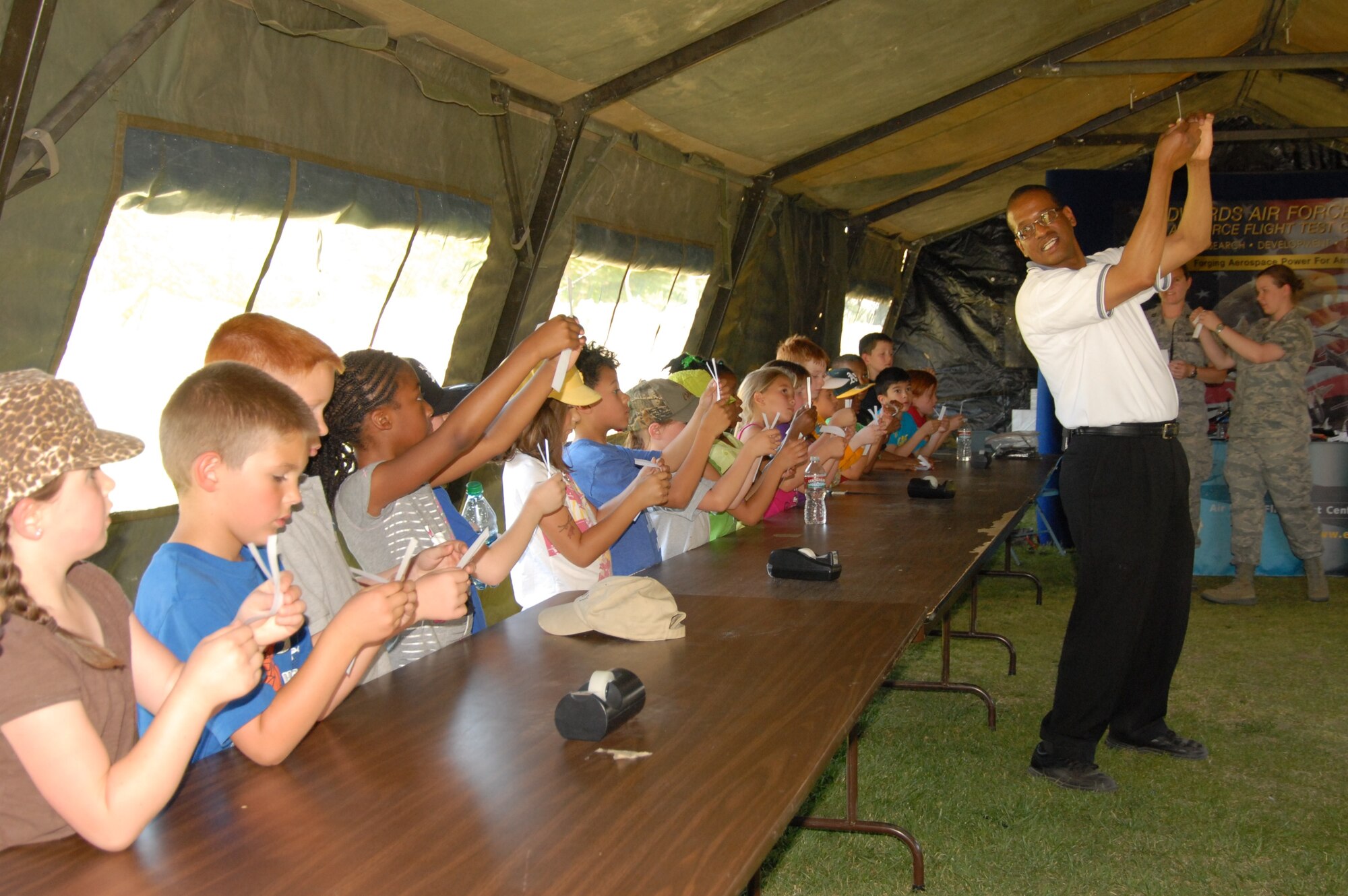 Branch Elementary students make paper helicopters under the direction of Mickey Bowen, Air Force Flight Test Center Engineering Flight Test Outreach lead. Mr. Bowen taught the students how a helicopter flies. After they folded their papers into a helicopter shape the students dropped them to see how they twirled to ground. Five tents set up by the 95th Civil Engineer division held interactive displays for the children during the 3rd Annual Branch Elementary School Science Carnival May 3. (Air Force photo by Kenji Thuloweit)