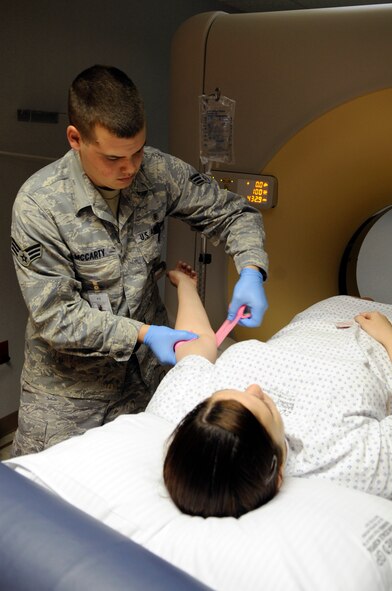 Senior Airman Sean McCarty, 2nd Medical Support Squadron radiology computed tomography technologist, bandages a patient after a CT exam of her abdomen and pelvis area. A CT scan provides a more in-depth look at an area than an X-ray. The CT provides a cross-sectional view, like bread slices, rather than an X-ray's two-dimensional view. (U.S. Air Force photo/Staff Sgt. John Gordinier)(RELEASED)