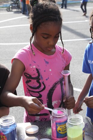 Gayla Hines, a Matthew C. Perry Elementary School second grader, pours sand into a tube to layer different colors into a design at the sand booth during the M.C. Perry Spring Fling School Carnival at the M.C. Perry Elementary School playground here May 13. Hines used more pink sand than any other color on the table for her sand design.