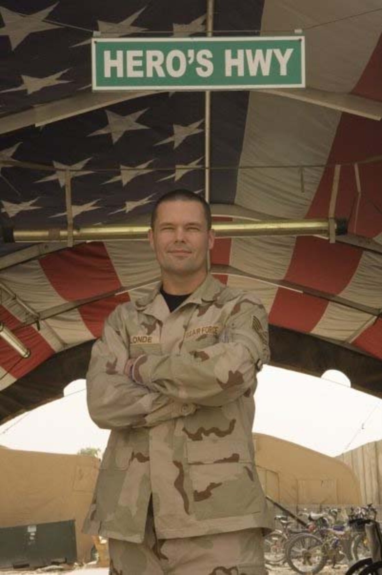 Tech. Sgt. Matthew Blonde poses at the entrance to Hero's Highway, Balad Air Base, Iraq, where the flag is posted on the inner roof a tent so injured troops can look up and know they are in an American area when brought in on litters seeking medical treatment. Sergeant Blonde, 452nd Aeromedical Staging Squadron, is a member of the Critical Care Aeromedical Transport Team and a full-time, civilian respiratory therapist.  (Photo courtesy of TSgt. Matt Blonde)