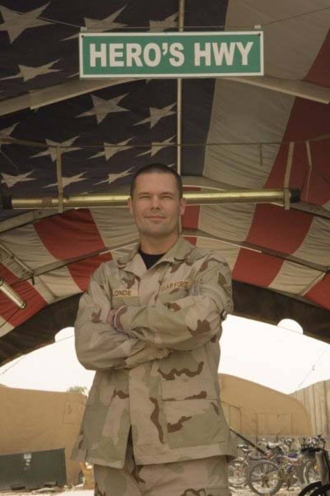 Tech. Sgt. Matthew Blonde poses at the entrance to Hero's Highway, Balad Air Base, Iraq, where the flag is posted on the inner roof a tent so injured troops can look up and know they are in an American area when brought in on litters seeking medical treatment. Sergeant Blonde, 452nd Aeromedical Staging Squadron, is a member of the Critical Care Aeromedical Transport Team and a full-time, civilian respiratory therapist.  (Photo courtesy of TSgt. Matt Blonde)