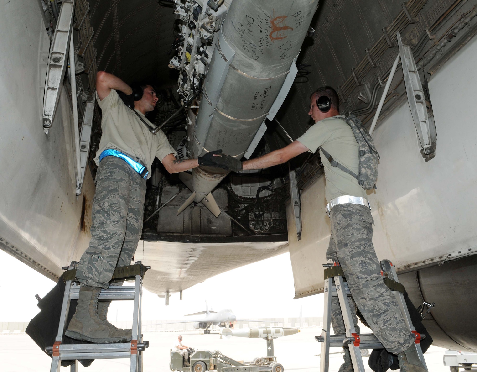 Staff Sgt. John Quiggle and Senior Airman Andrew Pippen from the 379th Expeditionary Aircracft Maintenance Squadron work hand in hand while loading munitions May 12 in Southwest Asia. Sergeant Quiggle and Pippen are both deployed here from Ellsworth Air Force Base, S.D. (U.S. Air Force photo/ Staff Sgt. Anthony Graham)