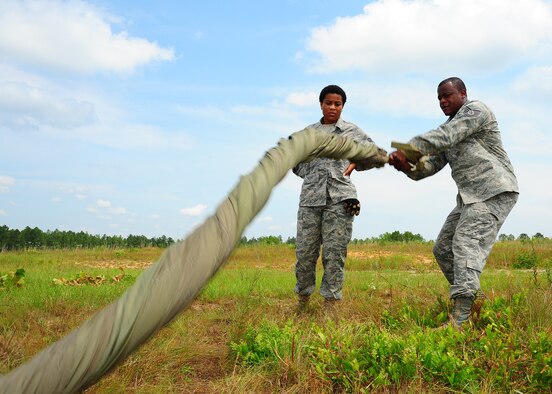 Tech. Sgt. Corey Gordon, 41st APS rigger, teaches Senior Airman Harriet Young, 41st APS, an easier way to "cigar roll" the G-12 equipment parachute. (U.S. Air Force photo by Staff. Sgt Yolanda Addison) 
