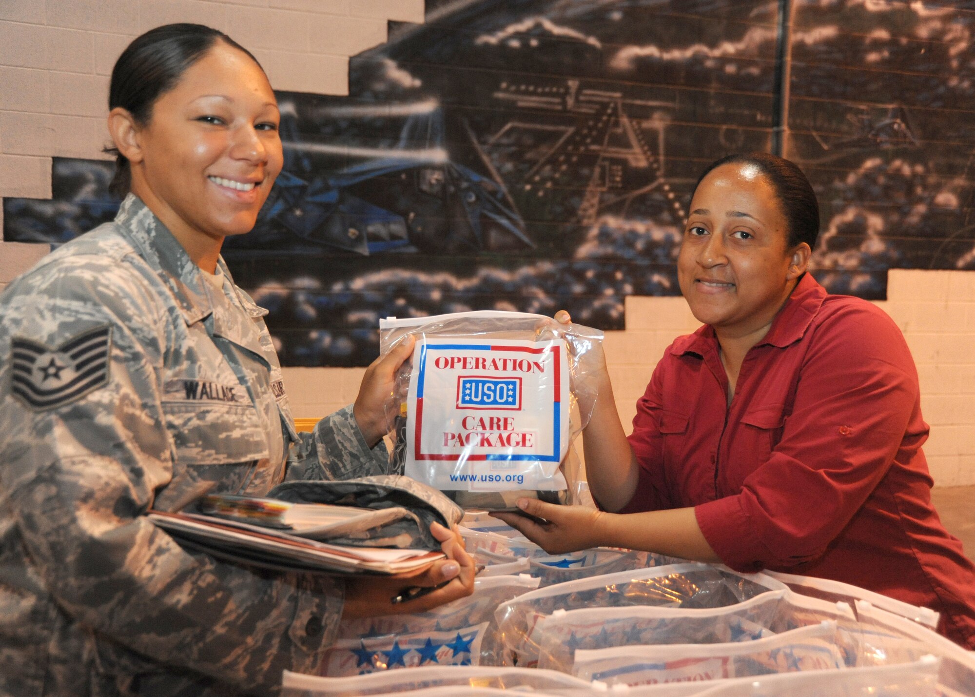 Tech Sgt. Alexis Wallace (left), an aircrew flight equipment technician with the 440 AW Operations Support Squadron, receives a USO care package from Stephanie Collier, a civilian personnel system manager at Pope Field, NC. The care packages consisted of a camouflaged toiletry bag, beef jerky and some treats for the long flight ahead. (U. S. Air Force  photo by Master Sgt. Kevin Brody)