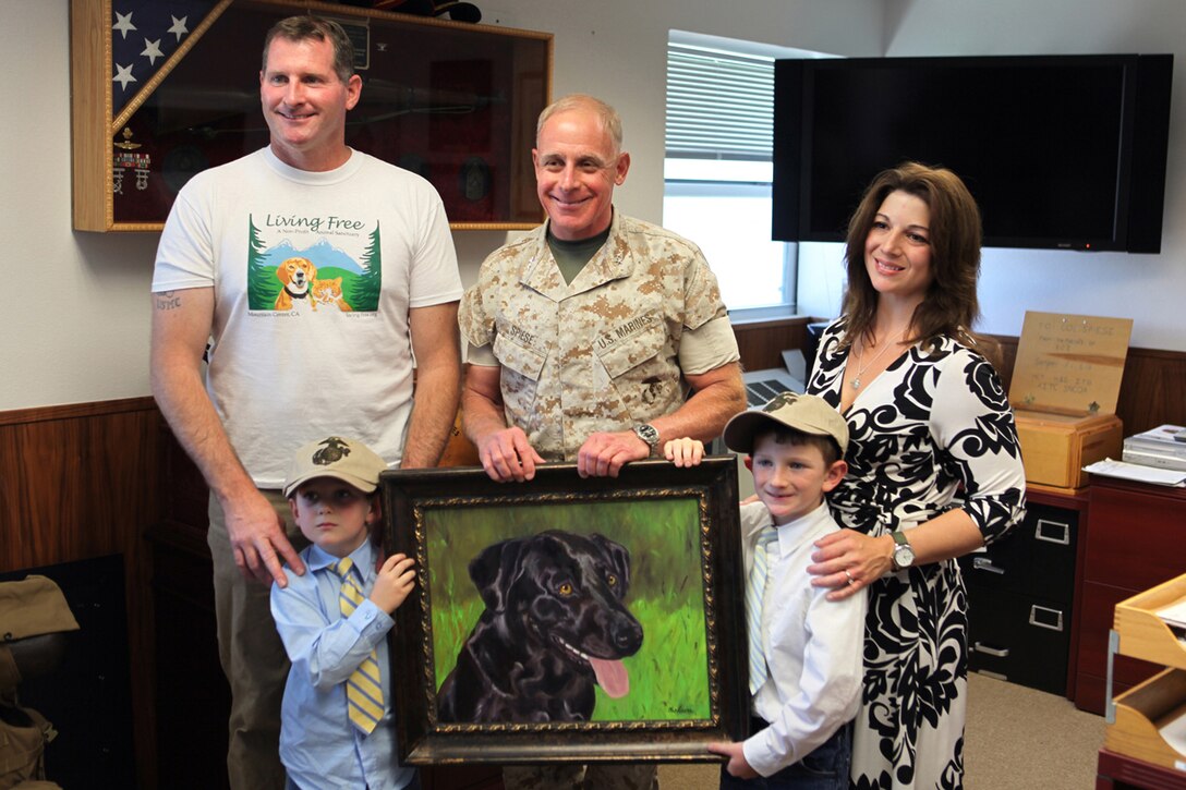 Caroline Carlson stands alongside her husband Steve her two children, Jake and Luke, as she presents a portrait she painted to Maj. Gen. Melvin G. Spiese, the Deputy Commanding General for I Marine Expeditionary Force, May 16. The painting depicts Sgt. Cole, a military working dog killed in combat.