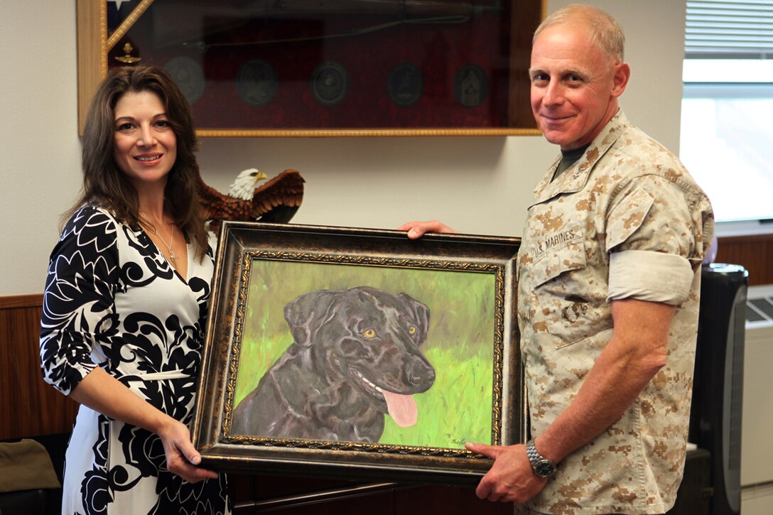 Caroline Carlson holds up a portrait with Maj. Gen. Melvin G. Spiese, the Deputy Commanding General for I Marine Expeditionary Force, during a presentation with Spiese. During the presentation Carlson explained what prompted her to paint the portrait of Sgt. Cole, a military working dog killed in Afghanistan.