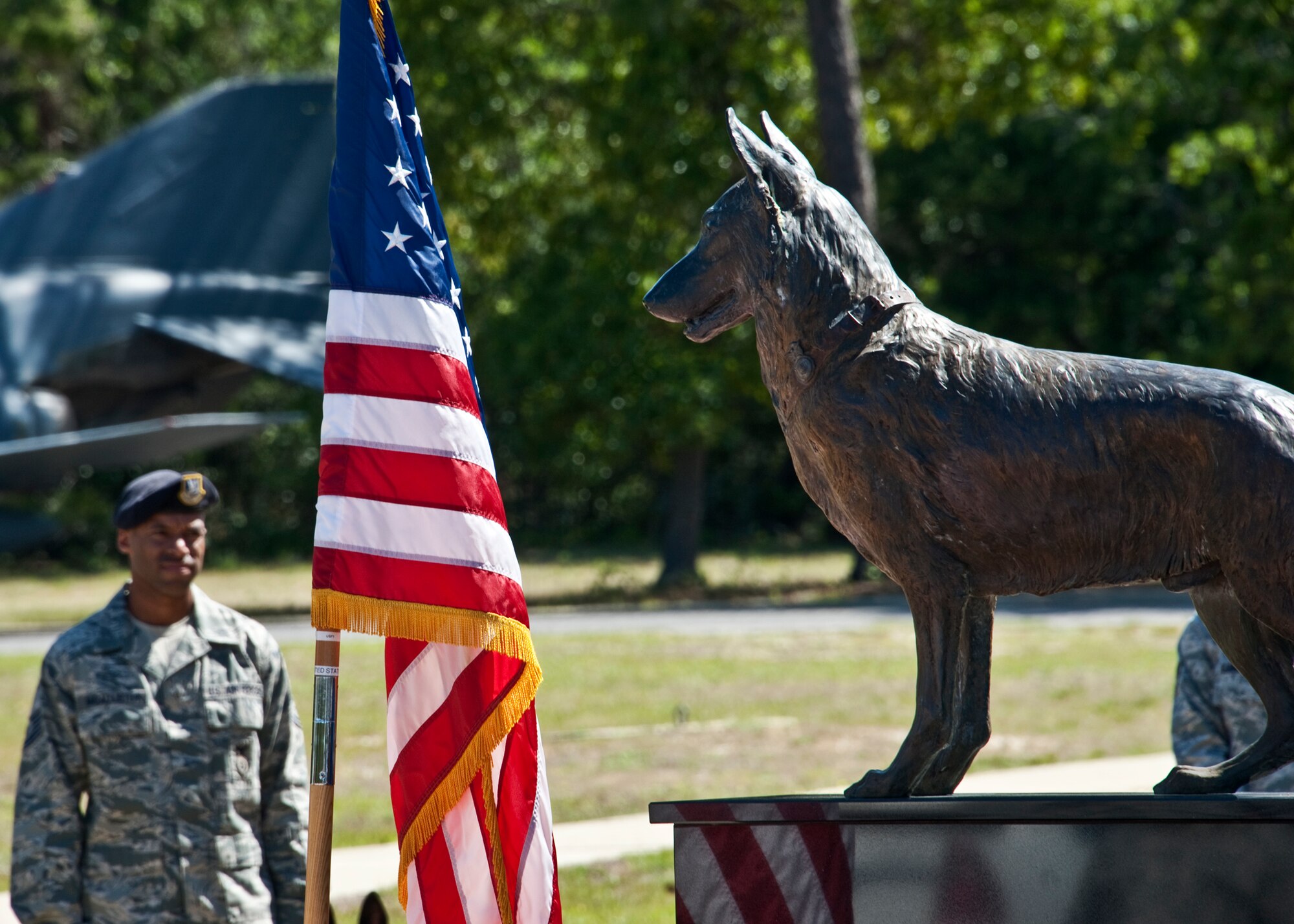 A security forces Airman stands with his military working dog behind the MWD memorial monument during a ceremony May 17 at the Air Armament Museum.  The ceremony honored MWDs and civilian K-9 unit for their service and remembered those who’ve fallen.  The ceremony was just one of the events happened for Police Week.  (U.S. Air Force photo/Samuel King Jr.)    