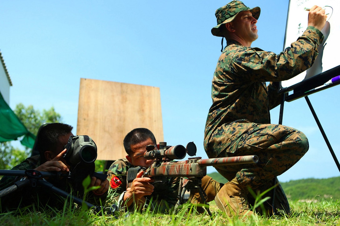Gunnery Sgt. Victor Lopez, the Scout Sniper Chief Instructor with Weapons Platoon, Landing Force Company, draws crosshairs on a board while Royal Thai Petty Officers 1st Class Ekapot Sengsie (left) and Nantawit Chunjan (right) get practice time as a sniper team May 12 at Sattahip Naval Base, here.