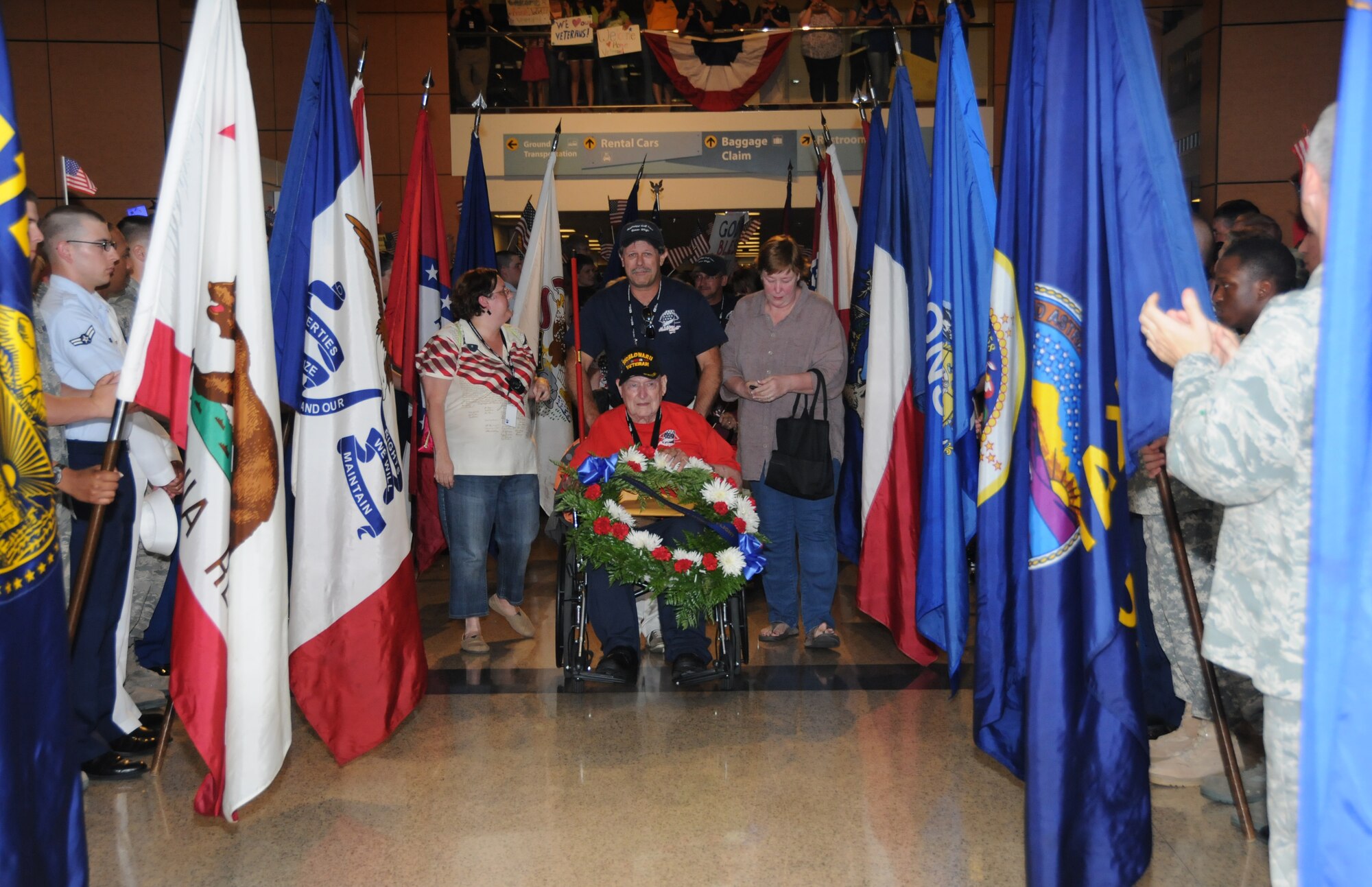 WorldWar II Navy veteran Sam Beatty of Biloxi passes through an aisle of state flags held by Keesler students at the Gulfport-Biloxi RegionalAirportMay 11 as he and 90 other war veterans returned from Mississippi’s first Honor Flight toWashington, D.C. Standing from left, Mr. Beatty is accompanied by Honor Flight officer JenniferWalton, volunteer Jeff Baldock and his daughter, Bridgette Aronson.  (U.S. Air Force photo by Kemberly Groue)