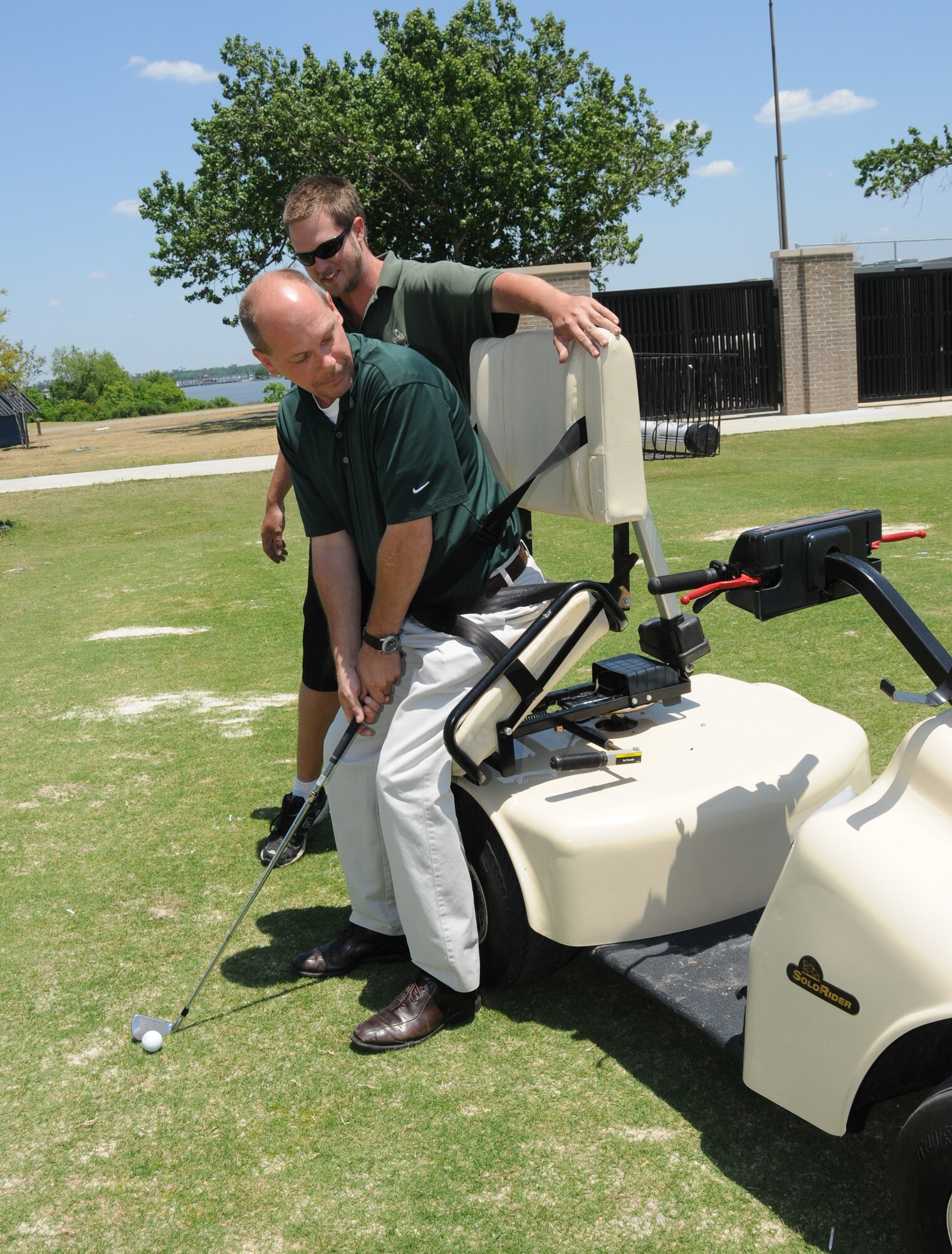 Luke Rooney, Bay Breeze Golf Course golf pro, adjusts the seat of the SoloRider 3400 to just the right spot to tee off.  Dominic Curtis, equipment technician, stands back to observe and assist.  (U.S. Air Force photo by Kemberly Groue)