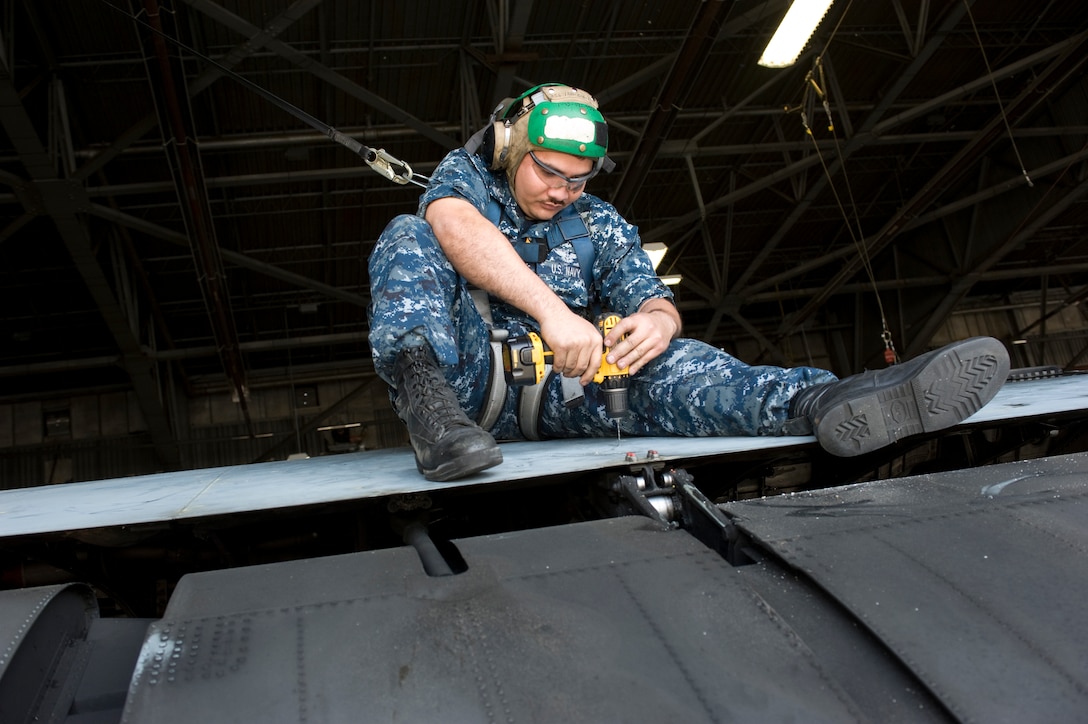 Navy aviation structural mechanic 2nd Class Julius Rosario sits atop a squadron C-130 aircraft, drilling out rivets from the trailing edge of the wing May 17. Petty Officer Rosario is assigned to Naval Fleet Logistics Squadron 53 here. (Photo by Bobby Jones)