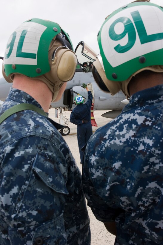 A Tactical Electronics Warfare Squadron 209 plane captain, center, gives signals to a squadron pilot during preflight operations as other VAQ-209 aircrew observe here May 17. The plane captain is responsible for launch and recovery of the squadron aircraft as the coordination of aircrew assigned to the aircraft mission. (Photo by Bobby Jones)