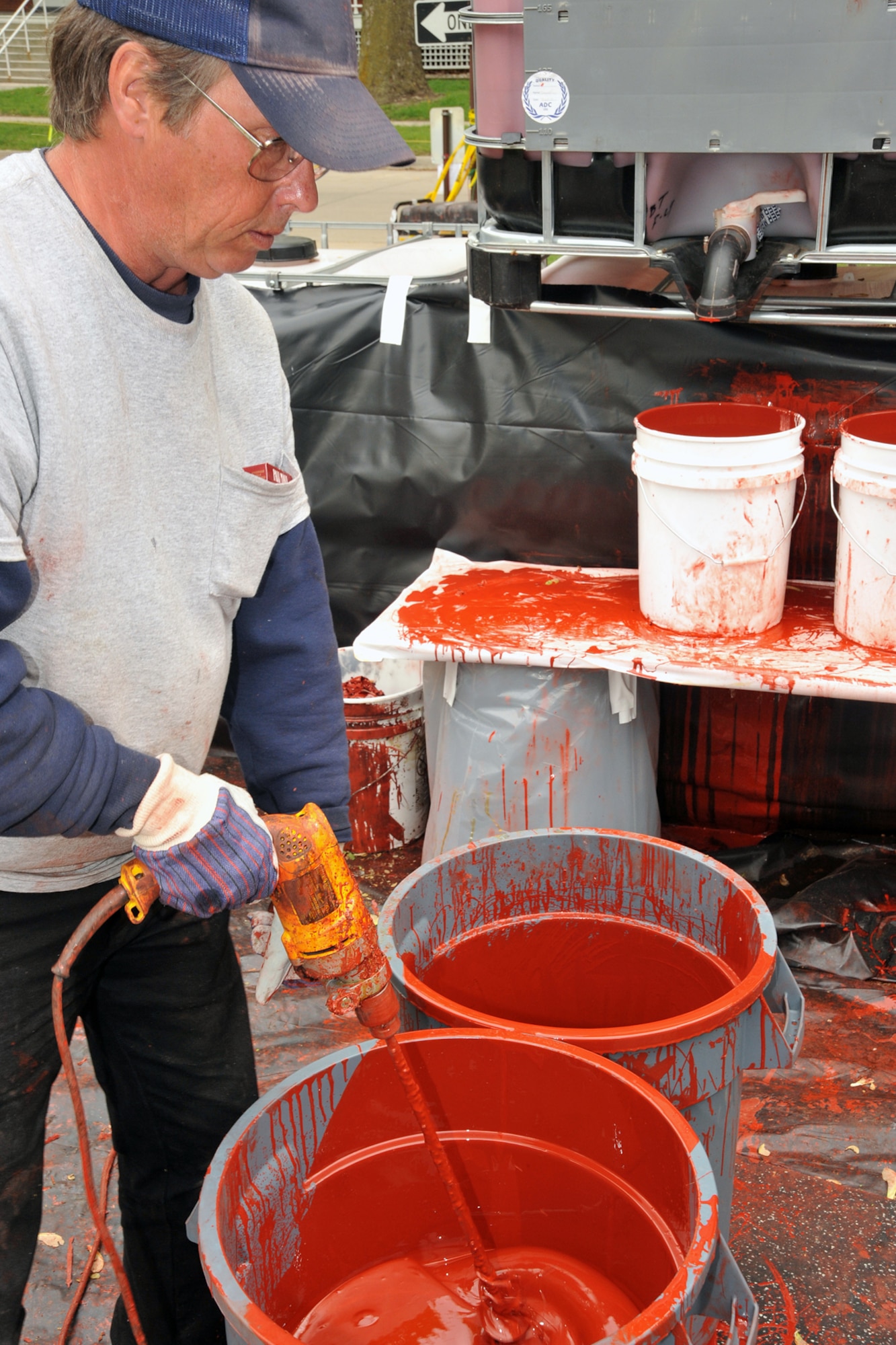 OFFUTT AIR FORCE BASE, Neb. -- Mark Hogan left, and Armon Niliaran of Bynon Sports, pours a bucket of top coat to be used as primer before laying a rubber surface on the track around the parade field at Offutt Air Force Base on May 18.  Bynon Sports, which is located in Hunt Valley, Maryland was contracted to cover the concrete track at the Offutt parade field with a rubber surface. U.S. Air Force Photo by D.P. Heard
