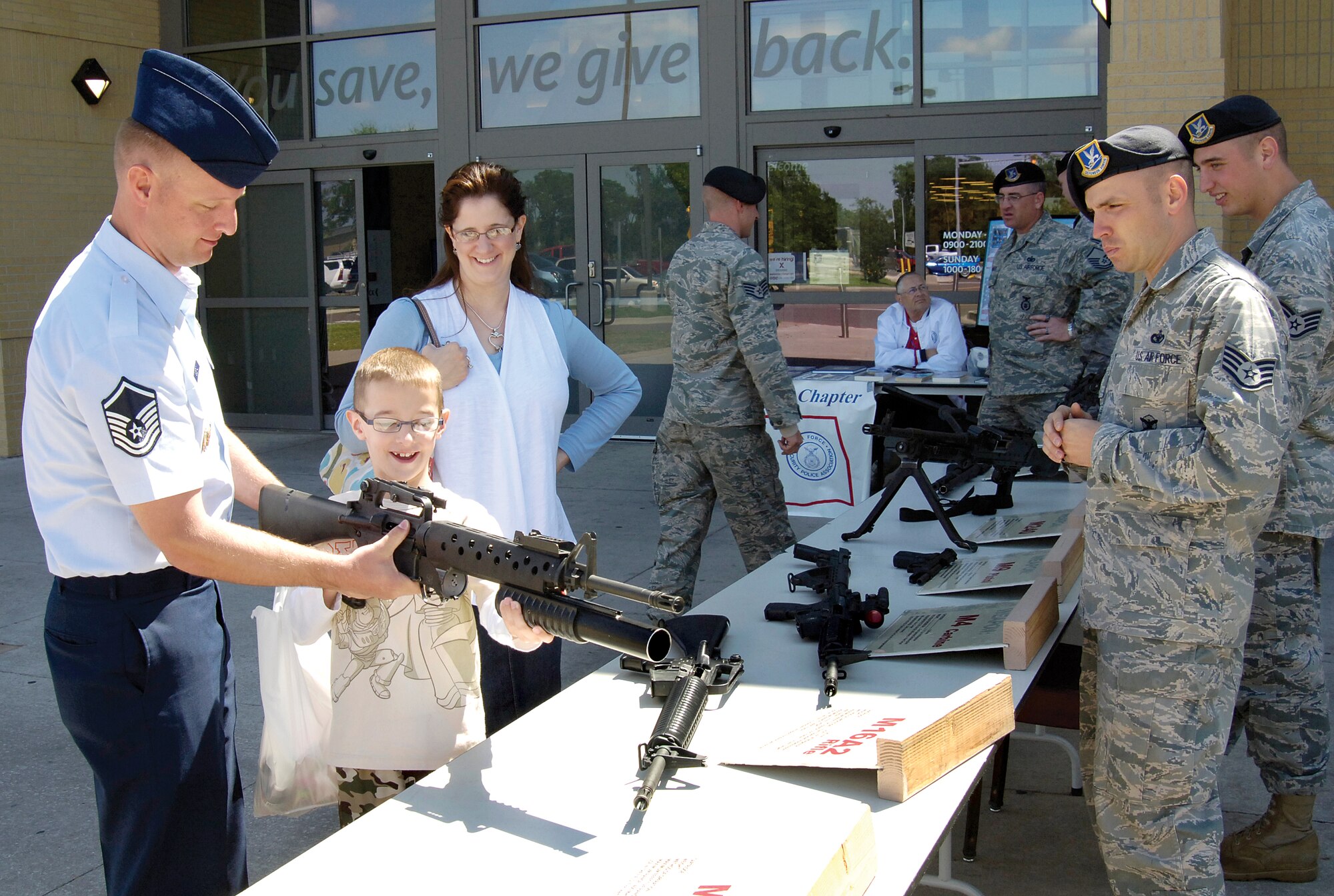 A table of military weapons attracts the attention of Exchange shoppers during Police Week activities May 16.  Master Sgt. Daniel Sigstad, an Oklahoma City Air Logistics Center Aerospace Sustainment Directorate program manager, helps his son, Kevin, 8, get the feel of an M16A rifle with an M203 grenade launcher as mom Kathleen watches.  Staff Sgt. Chris Price and Staff Sgt. Ryan Spidell, right, were two Combat Arms members who volunteered at the display. (Air Force photo by Margo Wright)