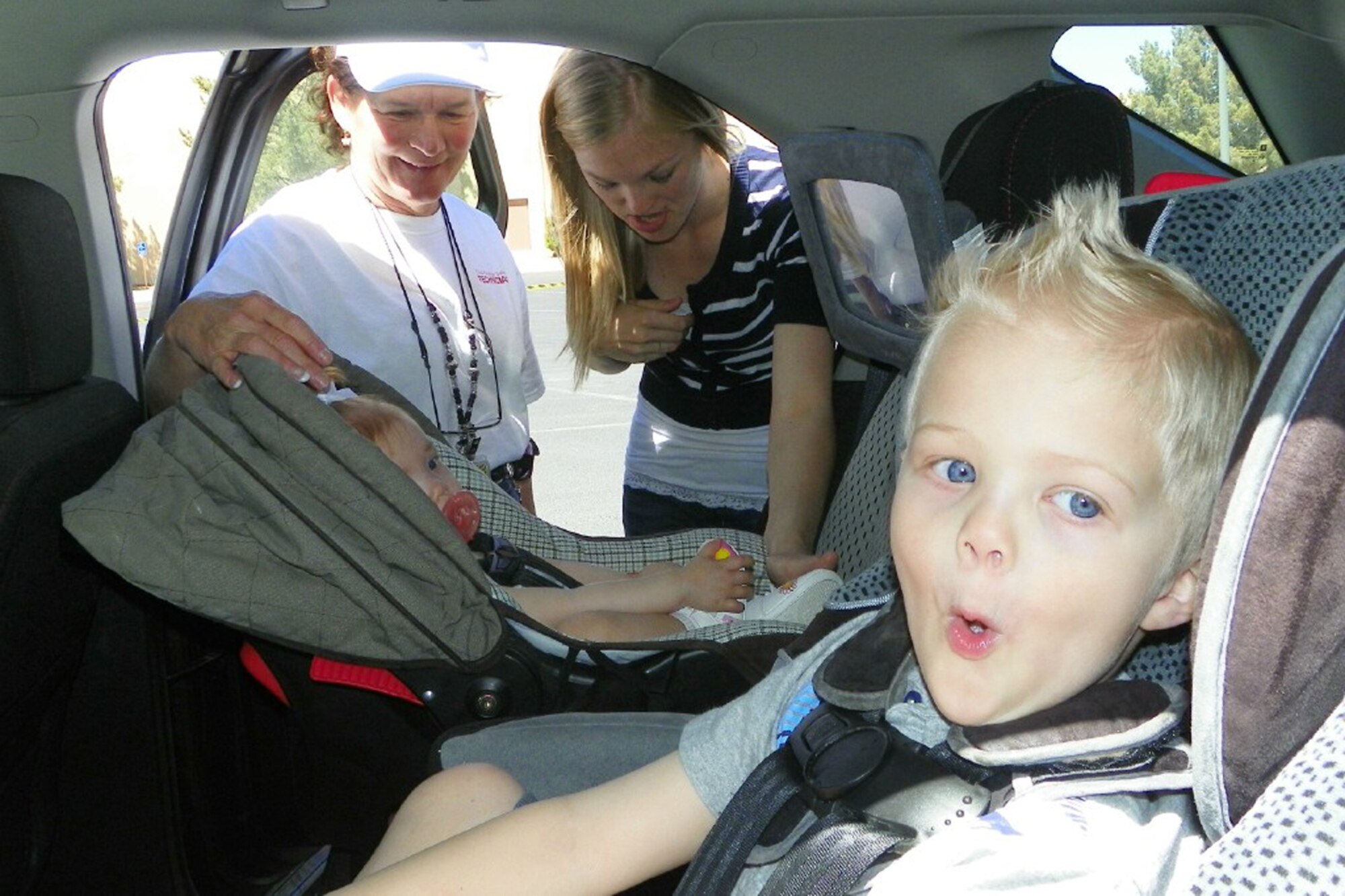 Ian Young, right, occupies his time making faces as his sister, Bailey, has her car seat inspected by child safety seat technician Dianne Keayes, left, of the Airman and Family Readiness Center and the children’s mother, Katie Young. Family Advocacy held a free car seat safety inspection April 29.  Courtesy Photo by Chrisan Smith