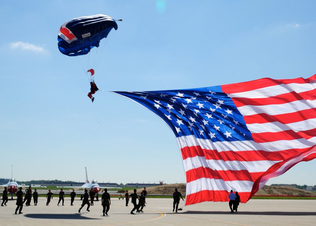 An E-Team Skydiver delivers the U.S. Flag to show center during the playing of the National Anthem at the 2011 Joint Service Open House Opening Ceremony here May 21. JSOH affords the public an opportunity to meet the men and women of the Armed Forces and to see military equipment from the Navy, Marines, Army, Air Force and Coast Guard. JSOH is planned and conduct through the efforts of active duty, guard and reserve servicemembers, as well as civilian employees, retirees and family members. (U.S. Air Force photo/ Staff Sgt. Nichelle Anderson)