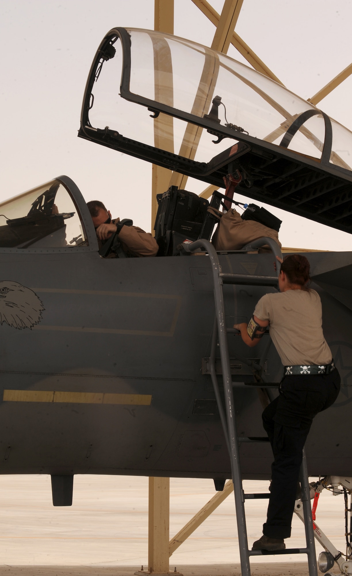 Airman 1st Class Caitlin MacKenzie, 380th Expeditionary Aircraft Maintenance Squadron crew chief, climbs up the ladder to assist the pilot with strapping into the F-15C Eagle, in Southwest Asia. The F-15 Eagle is an all-weather, extremely maneuverable, tactical fighter designed to permit the Air Force to gain and maintain air supremacy over the battlefield. Airman MacKenzie is deployed from Lakenheath AB, U.K. (U.S. Air Force photo by Senior Airman Maynelinne De La Cruz)