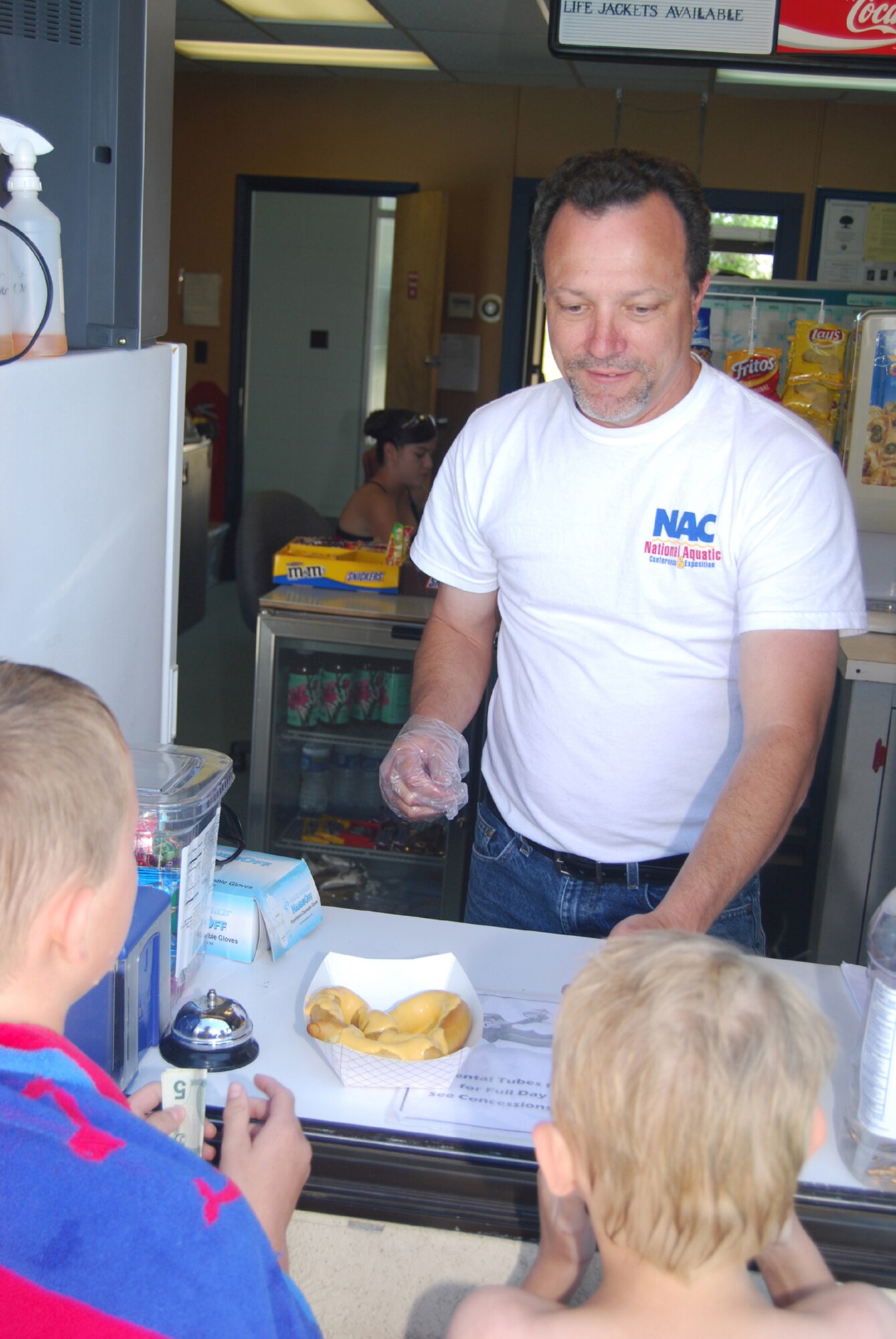 Steve Surls, 341st Force Support Squadron base pool manager, prepares a hot, cheesy pretzel for some pool-goers. The pool features a concession stand with popsicles, hot pretzels, nachos, drinks and other snacks to enjoy. (U.S. Air Force photo/Senior Airman Kristina Overton) 