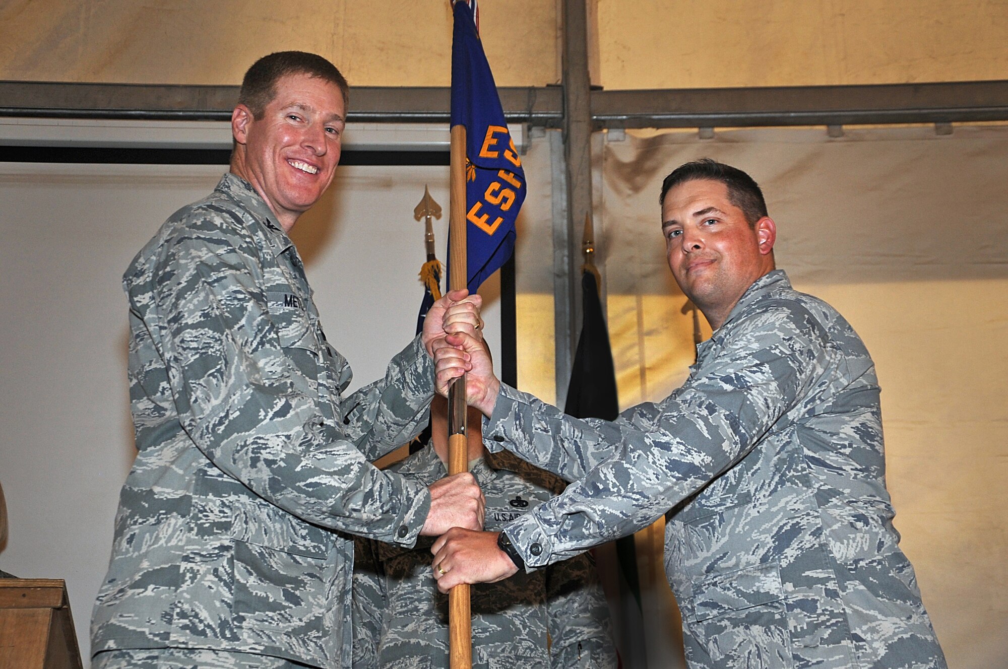 Colonel Tal Metzgar, 387th Air Expeditionary Group commander, left, hands the 387th Expeditionary Support Squadron guide-on to Lt. Col. David Wilder, the new commander of the squadron, May 21 at an undisclosed air base in Southwest Asia. Colonel Wilder took the 387th ESPTS reins from Lt. Col. Brian Weidmann in an official ceremony at the base. (U.S. Air Force photo by Senior Airman Cynthia Spalding)

