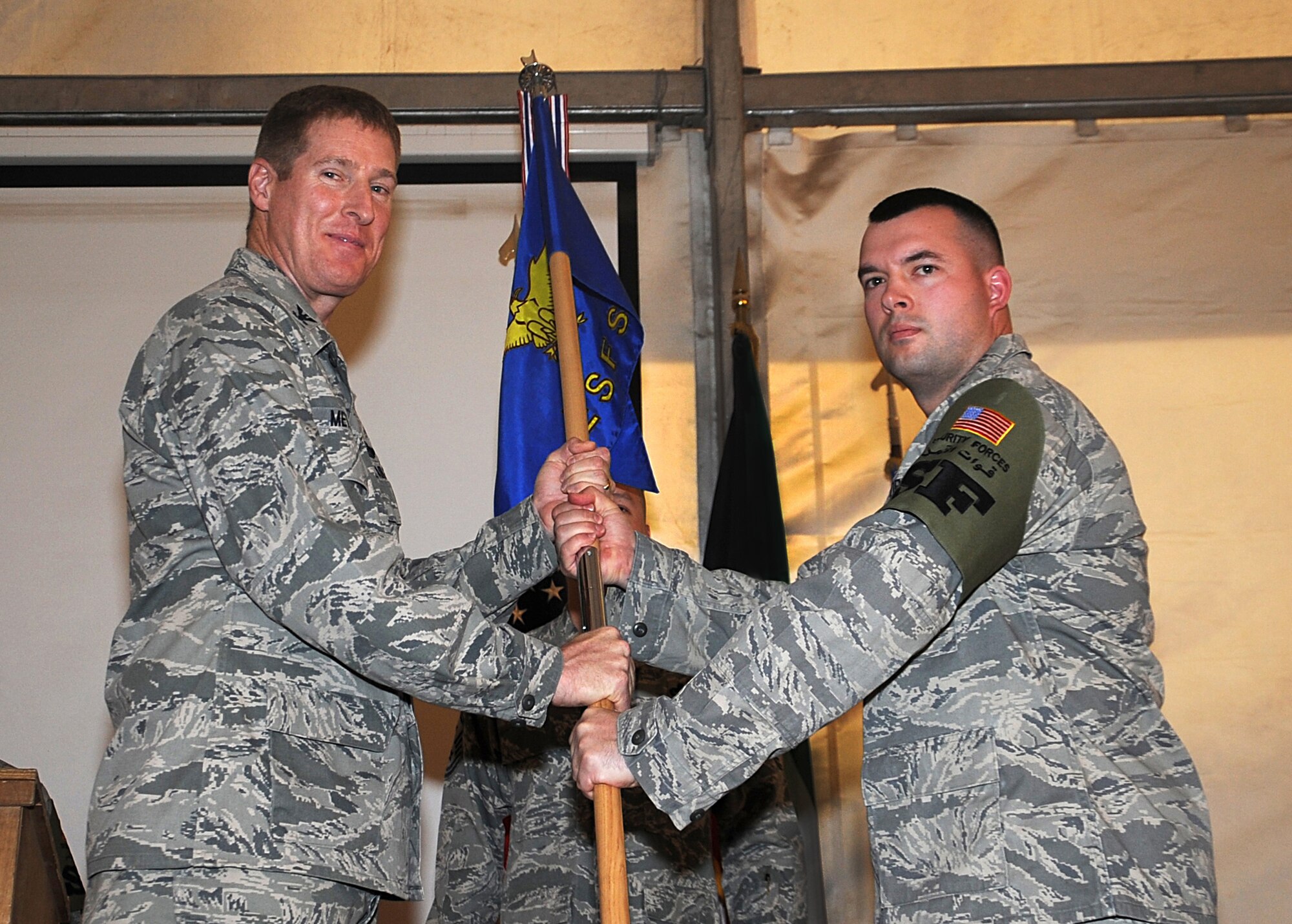 Colonel Tal Metzgar, 387th Air Expeditionary Group commander, left, hands the 387th Expeditionary Security Forces Squadron guide-on to Maj. Brian Quenette, the new commander of the squadron, May 21 at an undisclosed air base in Southwest Asia. Major Quenette took the 387th ESFS reins from Maj. Juan Silva in an official ceremony at the base. (U.S. Air Force photo by Senior Airman Cynthia Spalding)