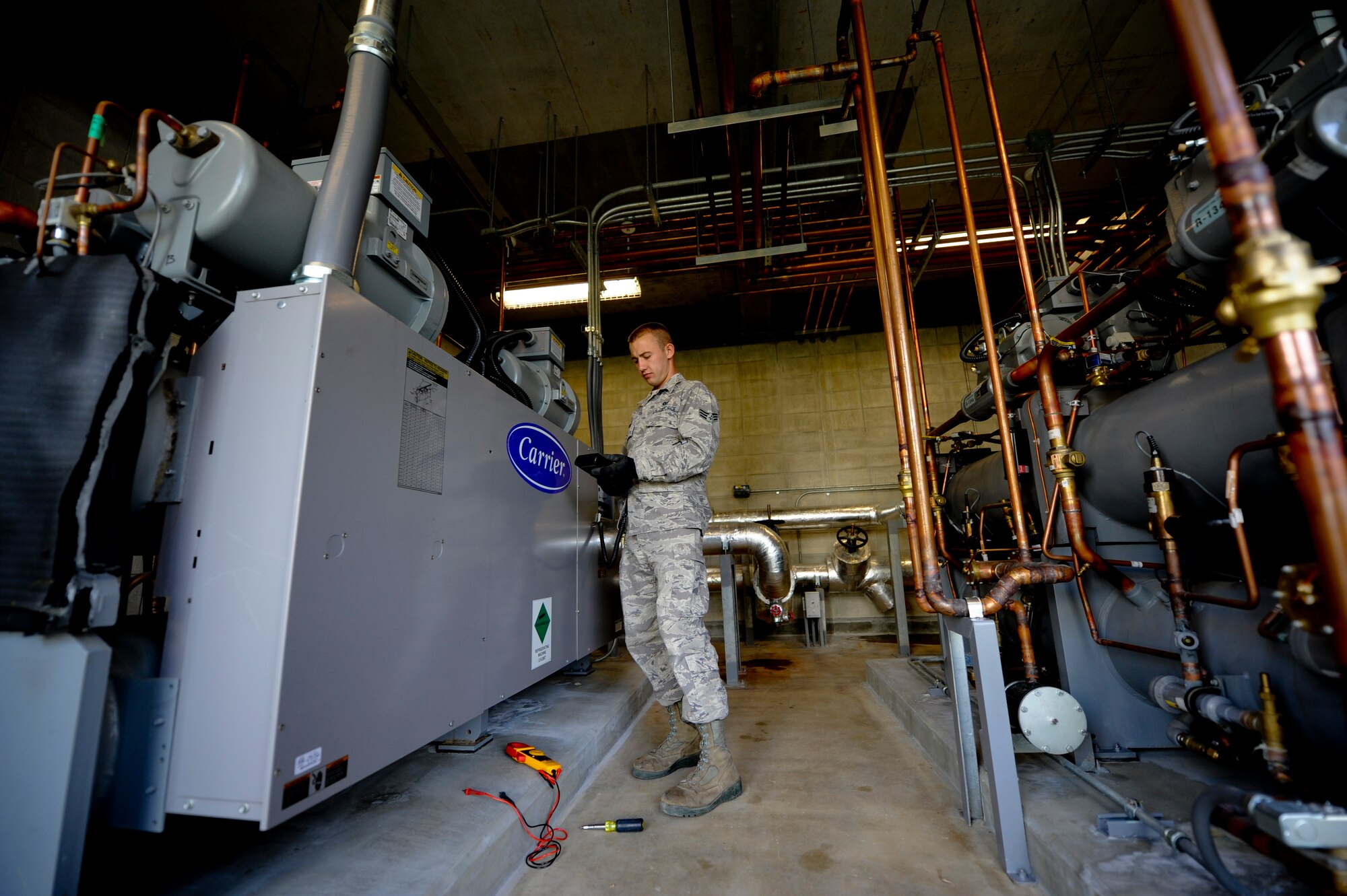 Senior Airman Derek Hunter, 18th Civil Engineer Squadron Heating, Ventilation, Air Conditioning and Refrigeration technician, thumbs through the remote control to a heating ventilation and cooling system April 21. In the past, Kadena’s HVAC/R shop has had to replace large, outdoor, energy-wasting chiller units for buildings’ AC systems on military installations across the island nearly every three years. Now,  Kadena recently instituted an initiative through the Air Force Smart Operations for the 21st Century program to replace the antiquated, over-oxidizing equipment with protected, indoor chillers to save the Air Force money. (U.S. Air Force photo/Staff Sgt. Jonathan Steffen)