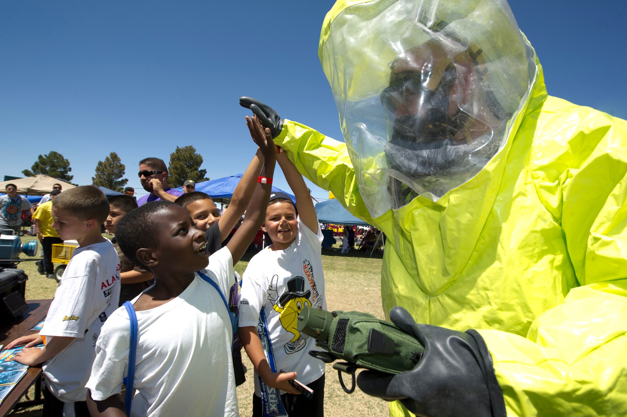 ALAMOGORDO, N.M. -- Airman 1st Class James Greenshields, 49th Civil Engineer Squadron, high-fives children participating in the three-on-three basketball tournament, May 21, 2011, held in conjunction with Armed Forces Day at Washington Park. Airman Greenshields wore a Level A hazardous material suit to demonstrate what members from the Emergency Management Flight are required to wear when coming into contact with chemical or biological agents, radiation, or a nuclear attack. (U.S. Air Force photo by Senior Airman Veronica Stamps/Released)