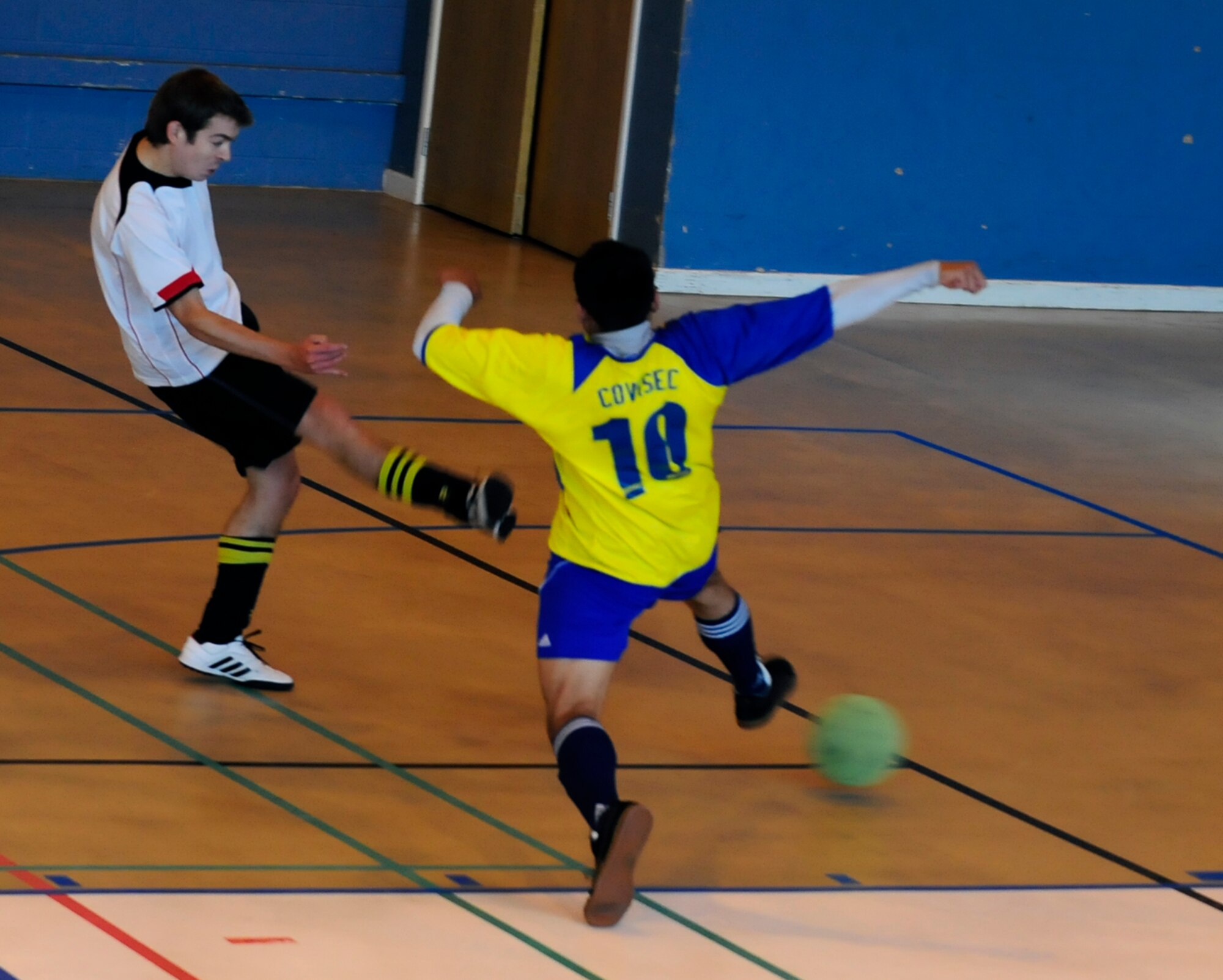 RAF MILDENHALL, England  -- Geoff Gough (white shirt), fires the ball home beyond Jhonatan Cardenas (10), to score his second and the 100th Civil Engineer Squadron’s fourth goal in their resounding 8-1 win in the  RAF Mildenhall Intramural Indoor Soccer Championship at the North Side Fitness Center, May 20, 2011. (U.S. Air Force photo/Senior Airman Ethan Morgan)