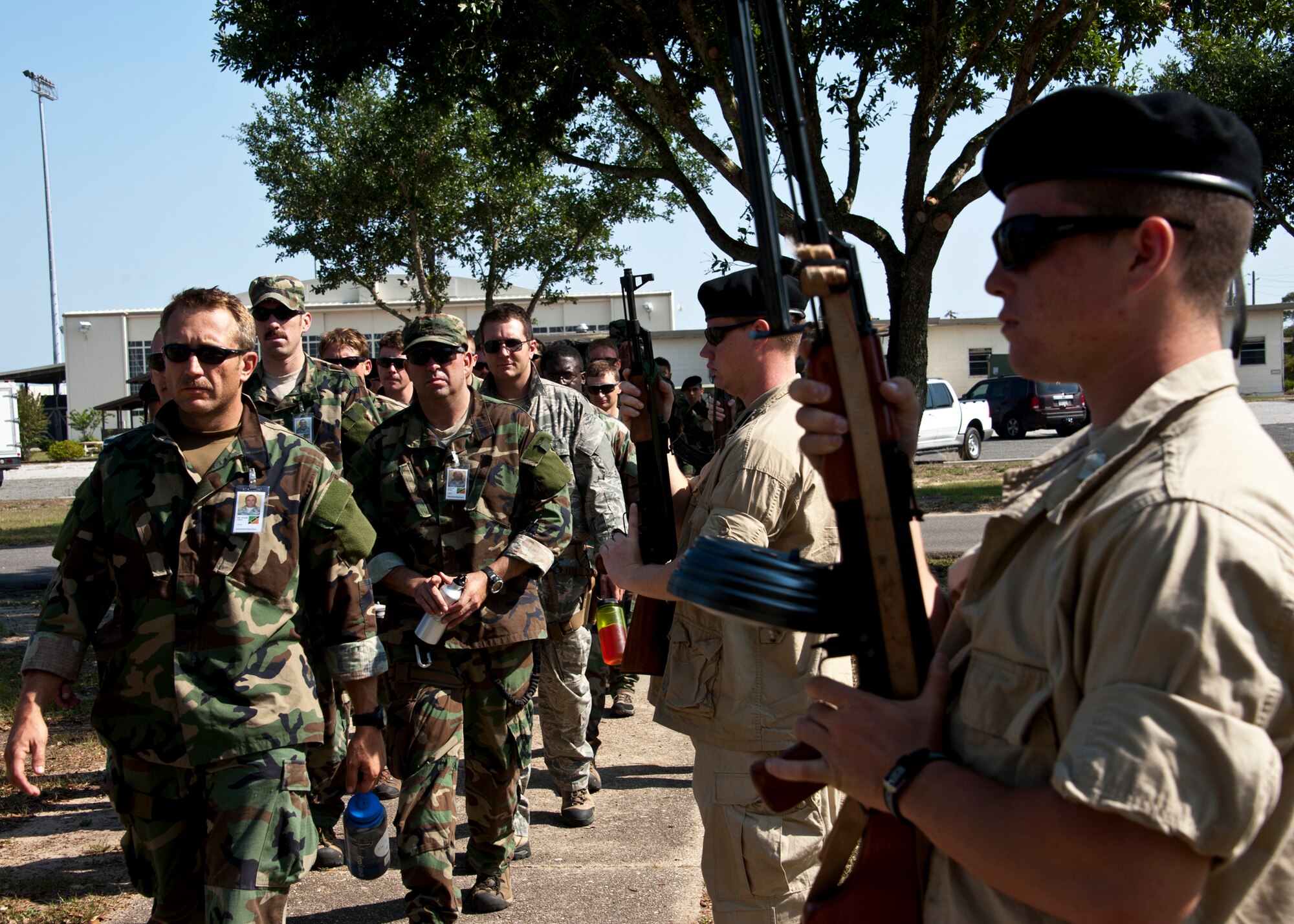 Combat Aviation Advisor students walk past soldiers toward their first meeting with the “simulated” partner-nation base leadership during the Raven Claw exercise, May 23 at Duke Field, Fla.  As part of the exercise, 19 CAA students deployed to a foreign nation to advise and train their air forces in fixed wing and rotary aircraft operations.  The four-day exercise is the capstone of 12 weeks of baseline certification training for CAA.  The year-long process to become a CAA also includes months of language and flight training.  (U.S. Air Force photo/Tech. Sgt. Samuel King Jr.)